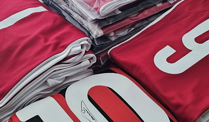 Stack of Ajax and AC Milan fanshop shirts prepared for a signing session, with a large “10” back number ready—clear behind-the-scenes proof of handling.