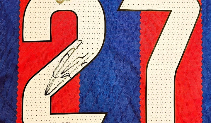 Close-up of an early signed Barcelona shirt by Lamine Yamal, featuring his autograph across the number 27 on the classic red and blue fabric.