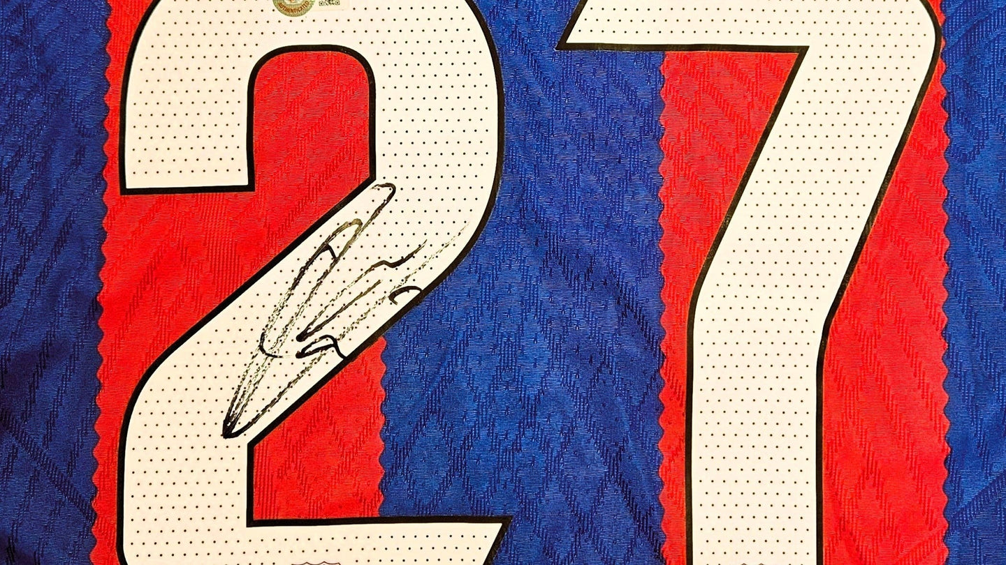 Close-up of an early signed Barcelona shirt by Lamine Yamal, featuring his autograph across the number 27 on the classic red and blue fabric.