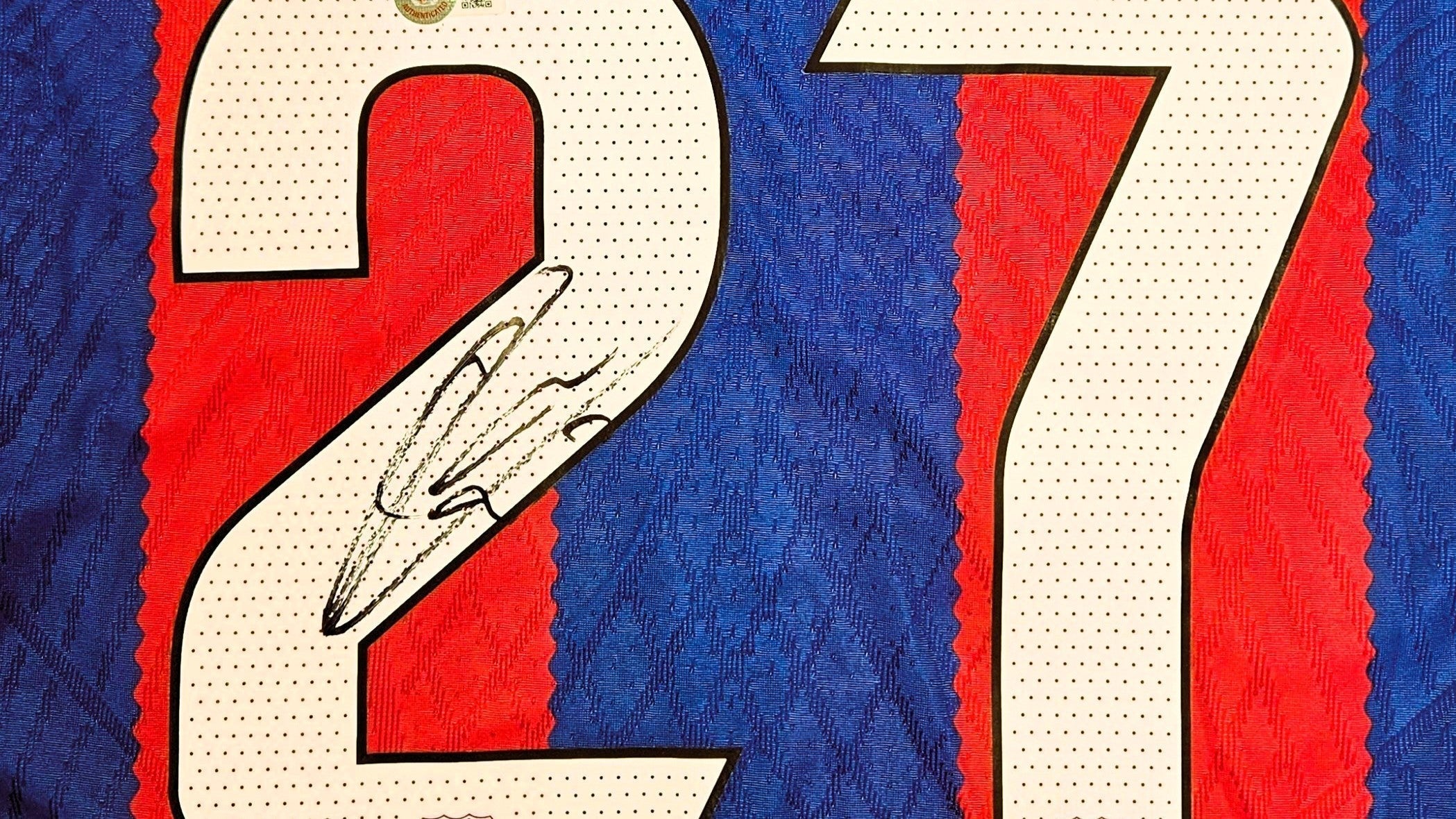 Close-up of an early signed Barcelona shirt by Lamine Yamal, featuring his autograph across the number 27 on the classic red and blue fabric.