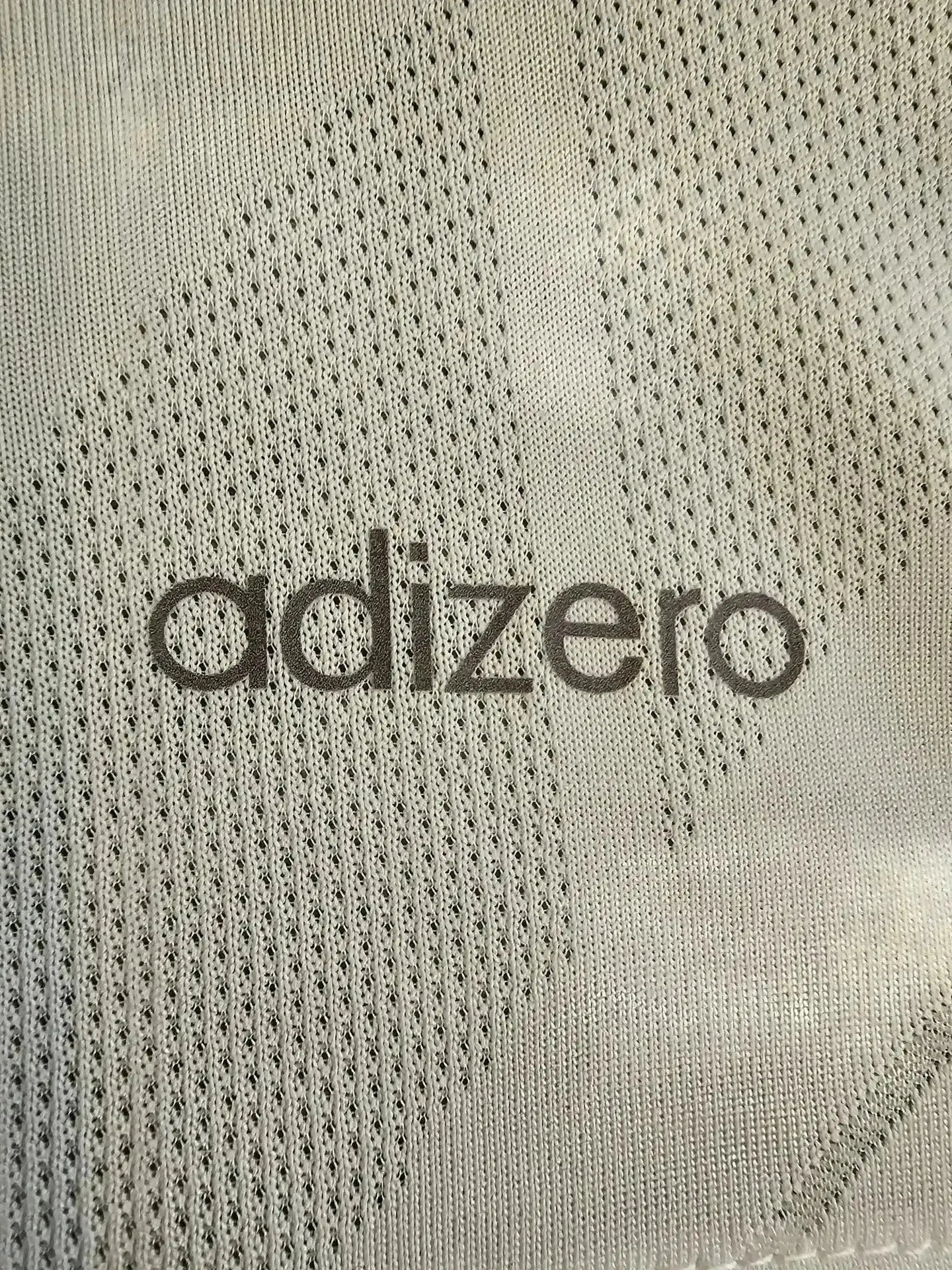 Close-up of adizero text on a gray patterned soccer jersey fabric.