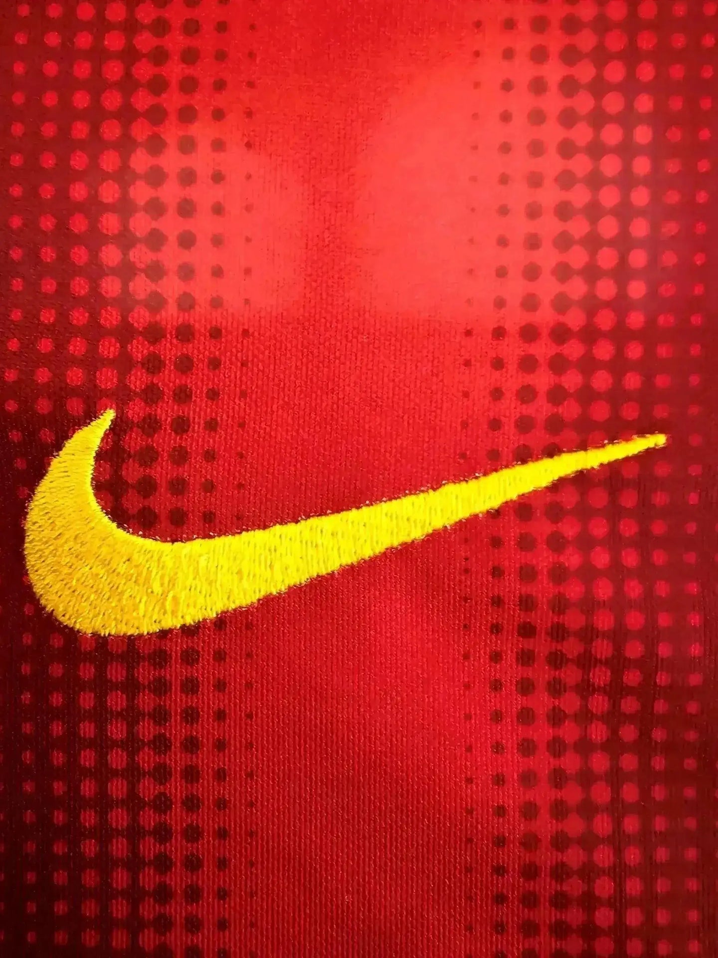 Close-up of yellow Nike swoosh logo on red fabric with dotted pattern.