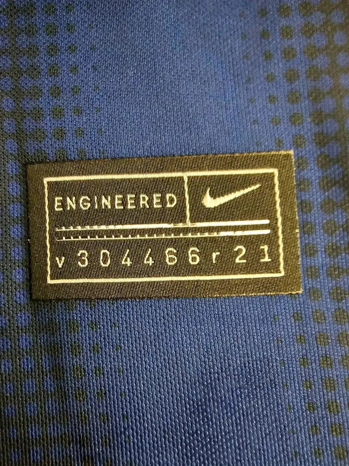 Close-up of Nike tag reading 'ENGINEERED v304466r21' on a blue fabric background.
