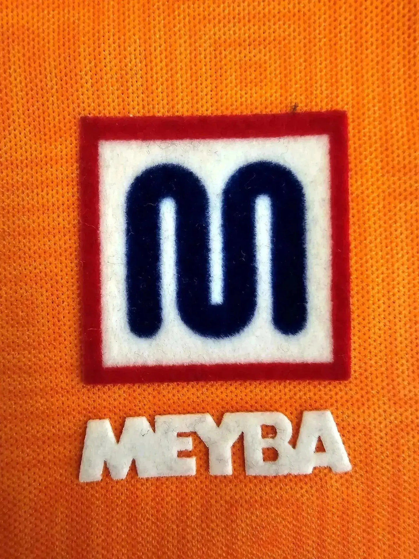 Crest detail featuring MEYBA and a prominent logo on an orange background.