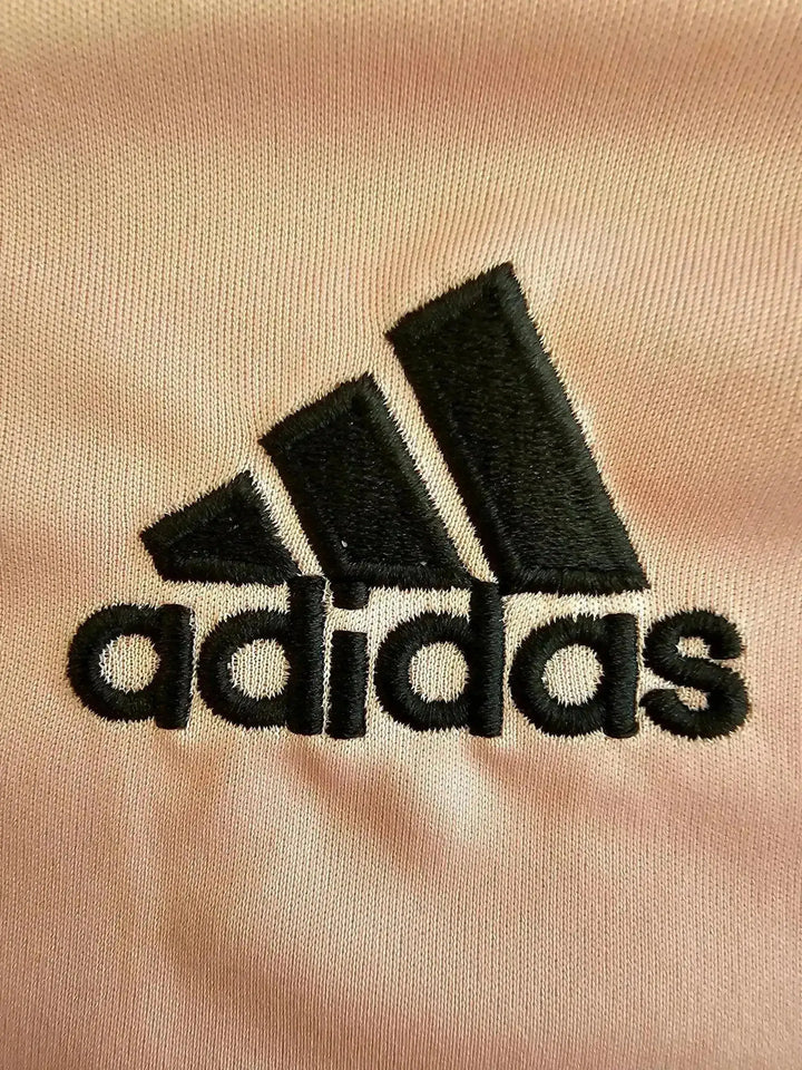 Close-up view of the embroidered black adidas logo on a light pink soccer jersey.