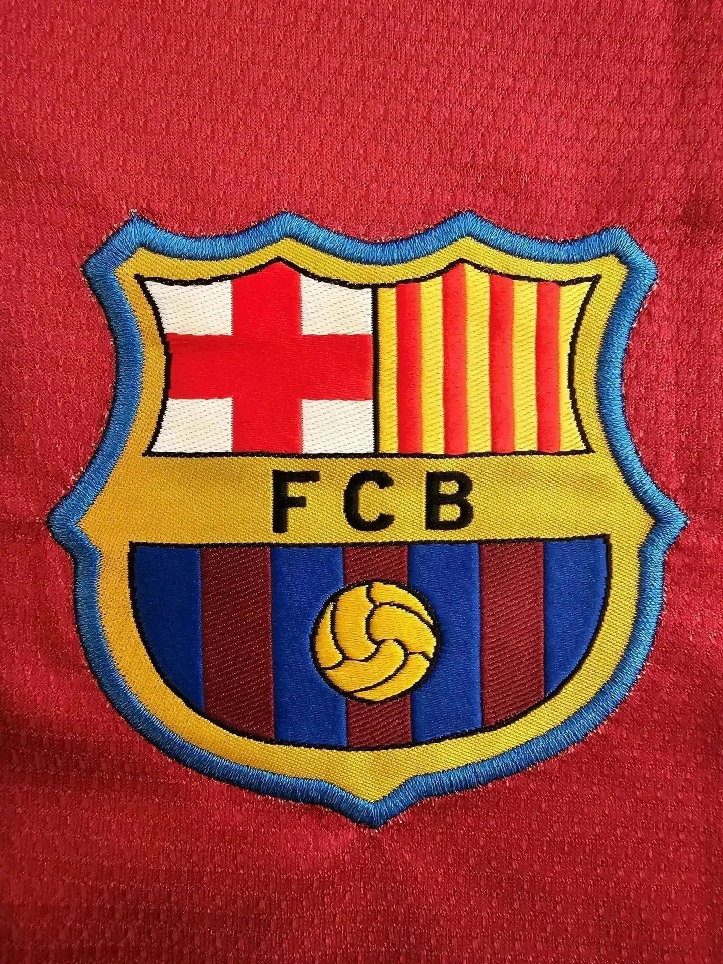 FC Barcelona crest detail featuring red and blue stripes with yellow accents and a central football.