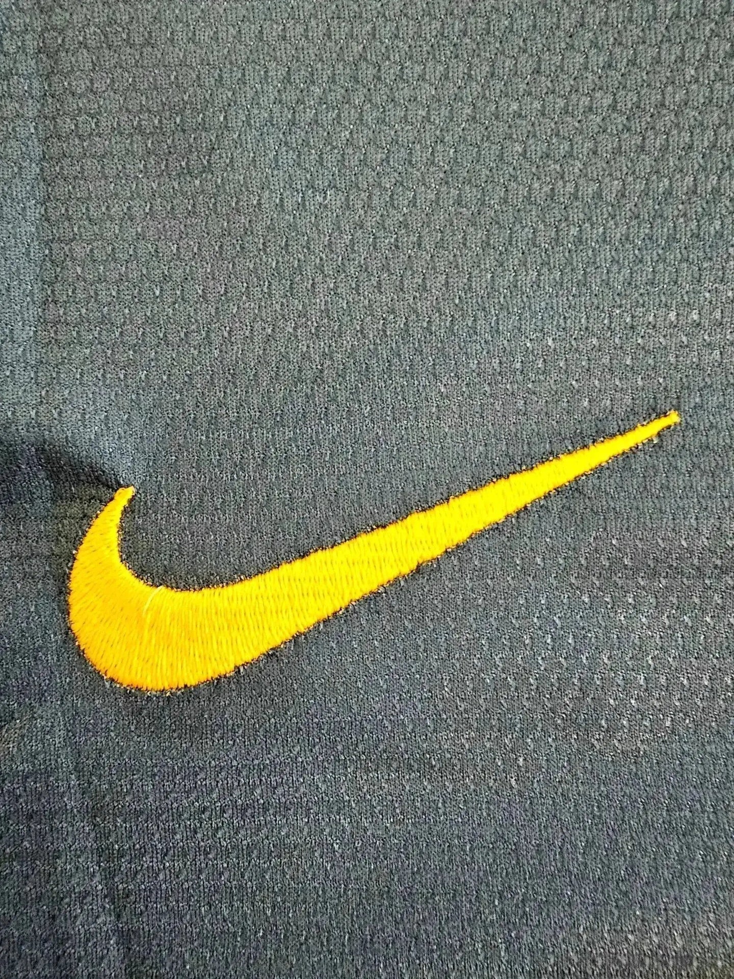 Close-up of Nike logo in yellow embroidery on dark fabric.
