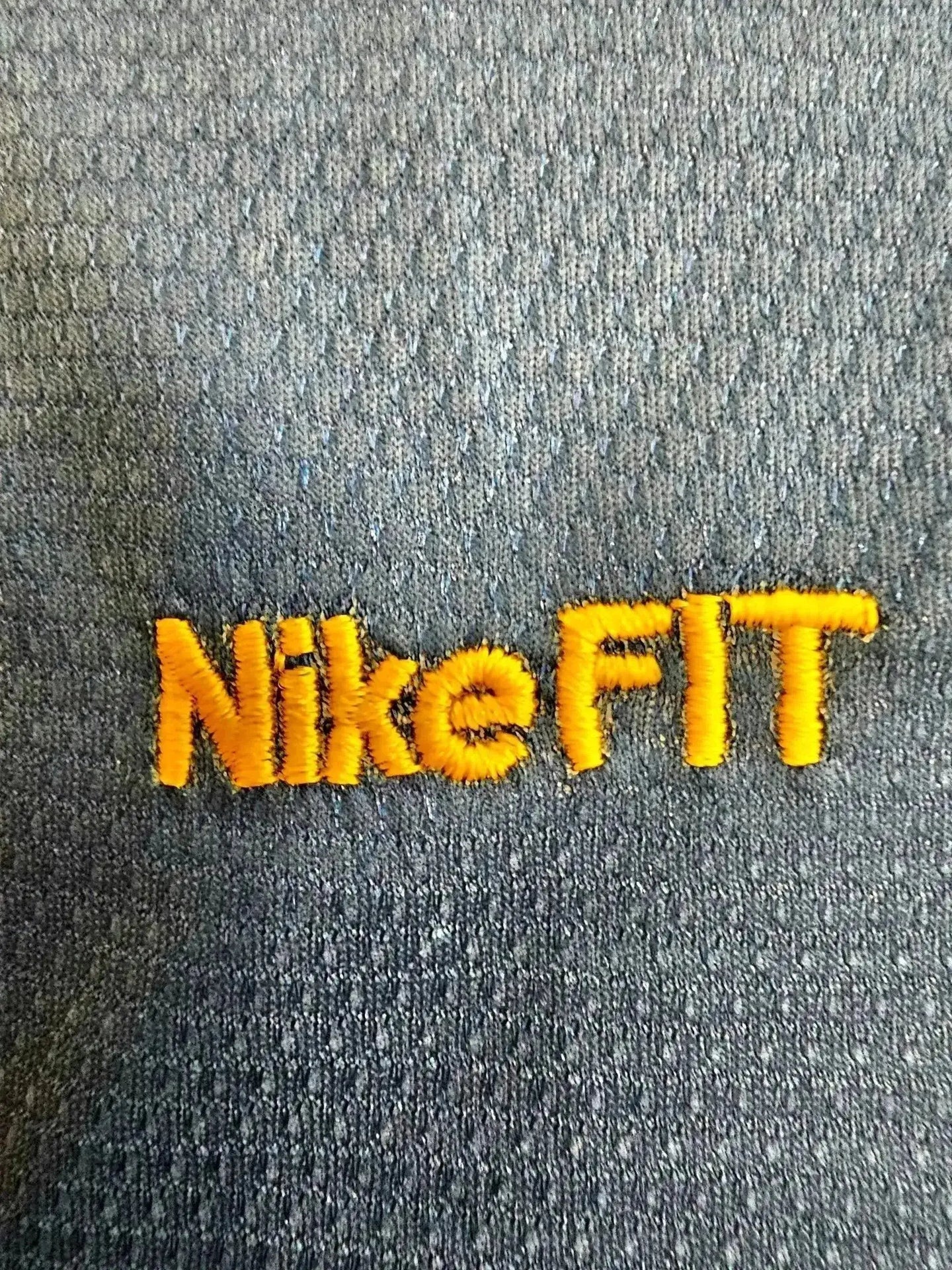 Close-up of the NikeFIT logo in orange stitching on a dark fabric background.