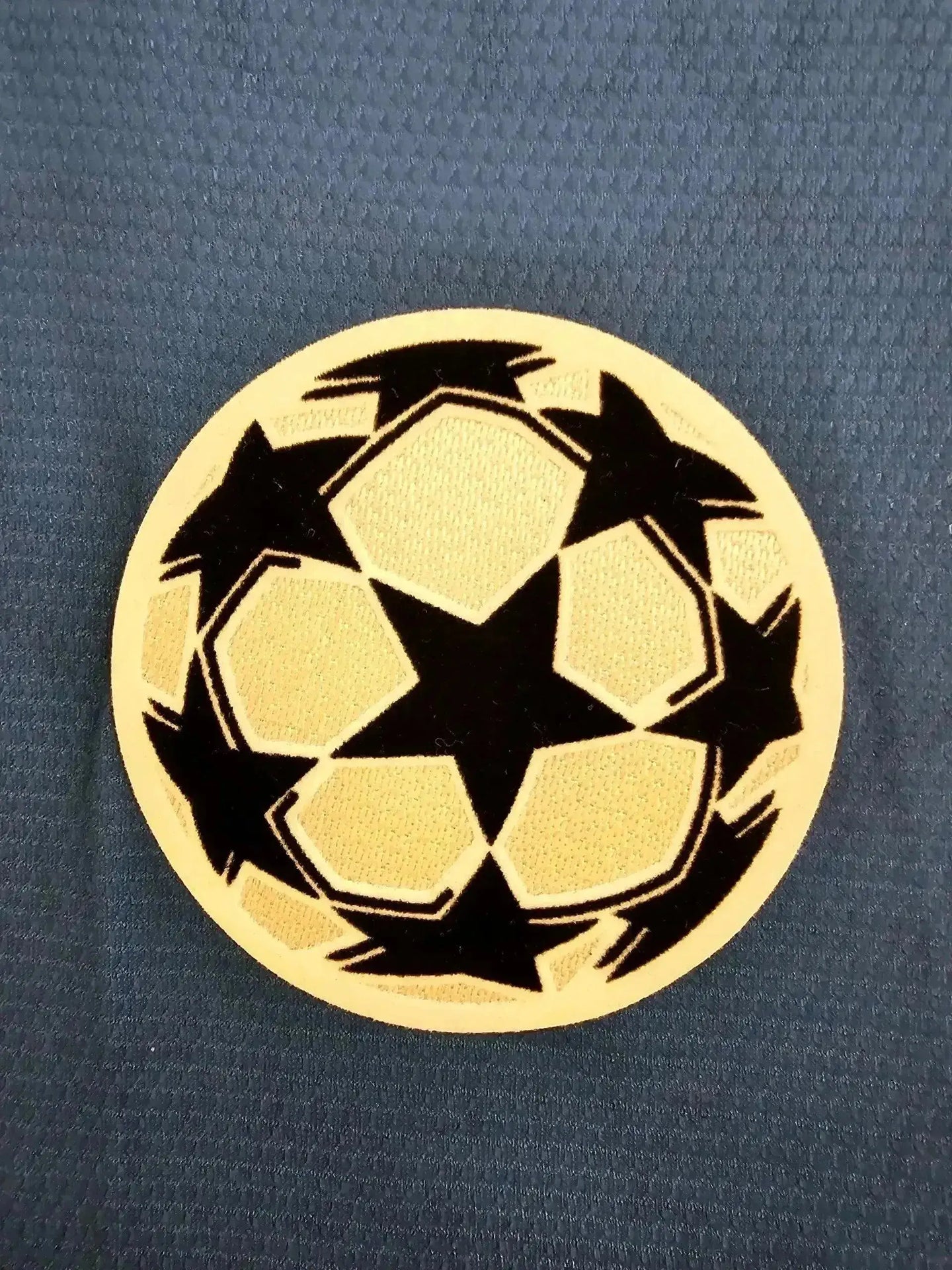 Crest detail featuring UEFA Champions League logo with black stars on a yellow background.