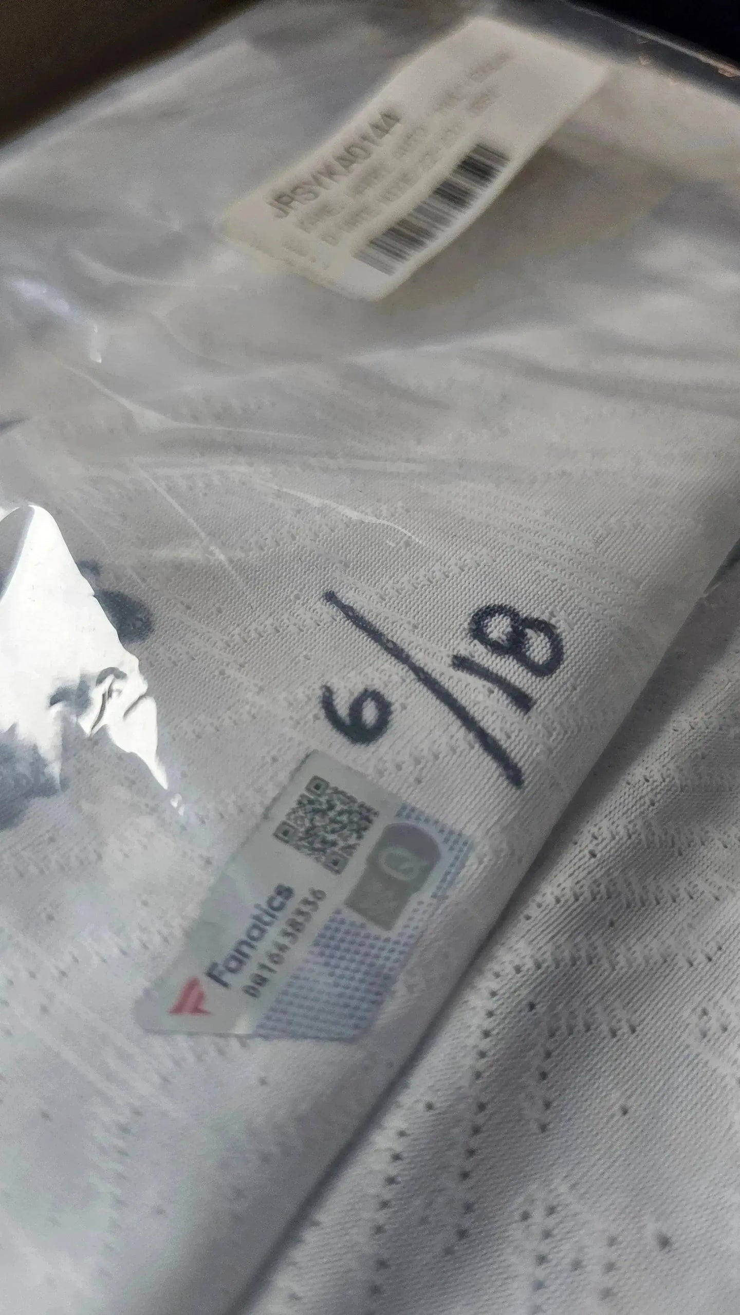 Detail showing fabric tag and inscription "6/18" on white soccer jersey.