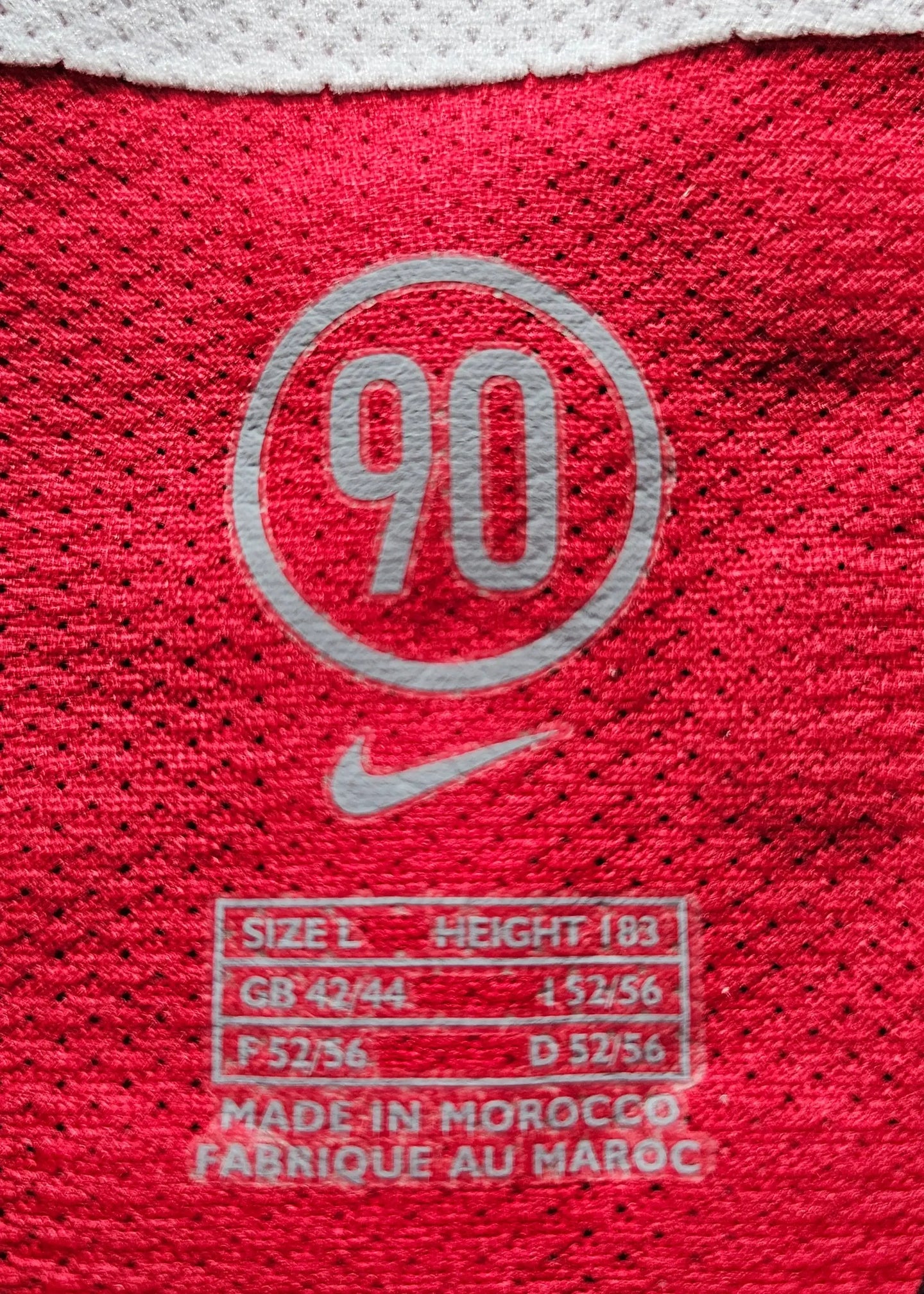 Detail showing '90' logo, Nike branding, and size information with red fabric background.