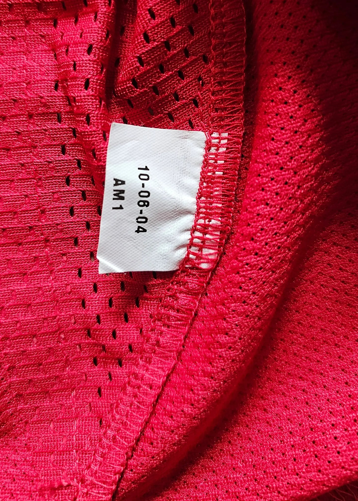 Red mesh fabric with care label showing text: 10-08-04 AM1.
