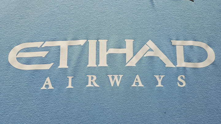 Close-up of the ETIHAD AIRWAYS sponsor print on Emmanuel Adebayor's sky-blue Manchester City shirt, with the Puma logo visible at the edge.