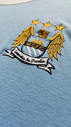 Manchester City FC logo on a light blue background