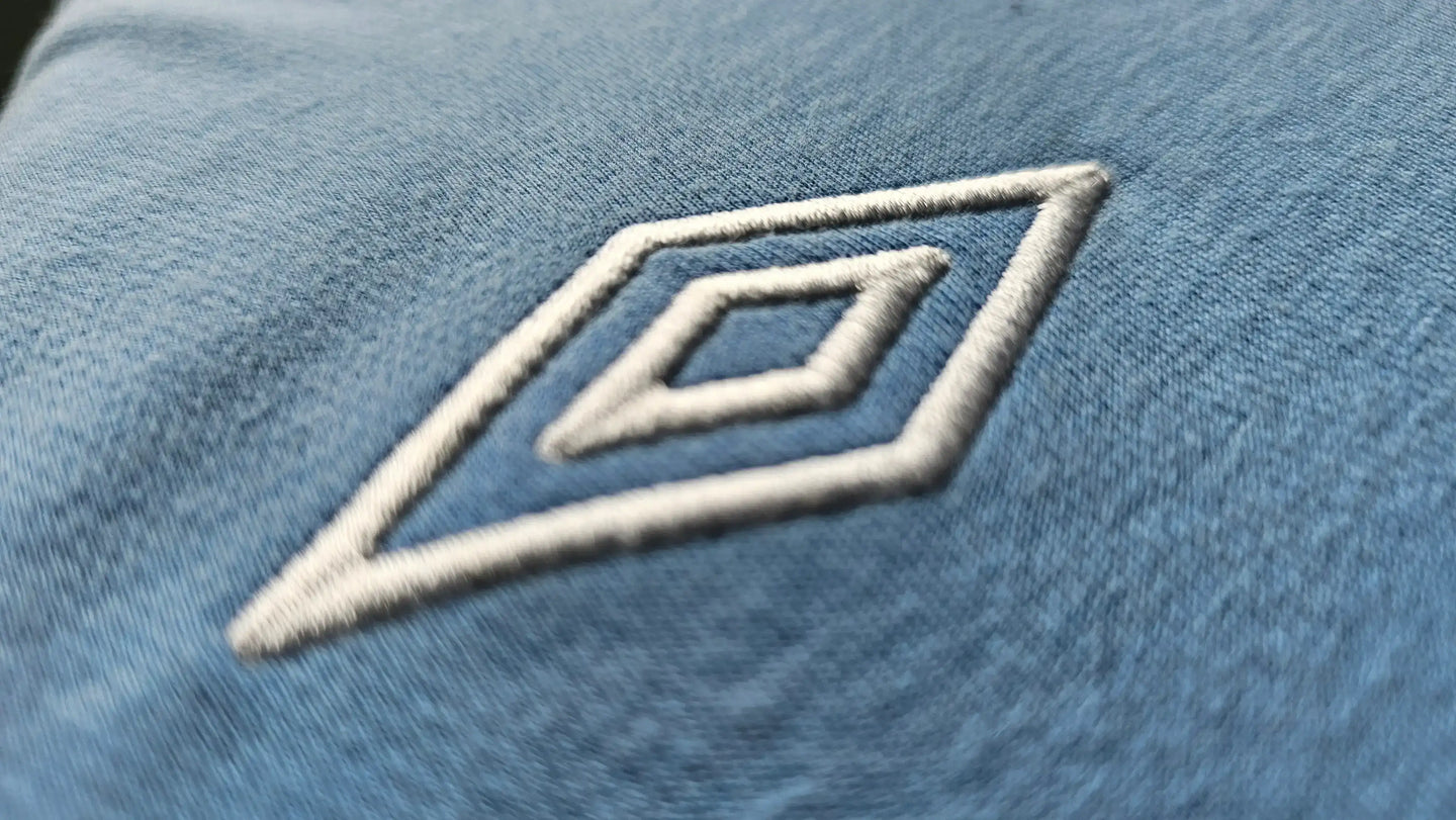 Close-up of the white Umbro logo on a blue soccer jersey.