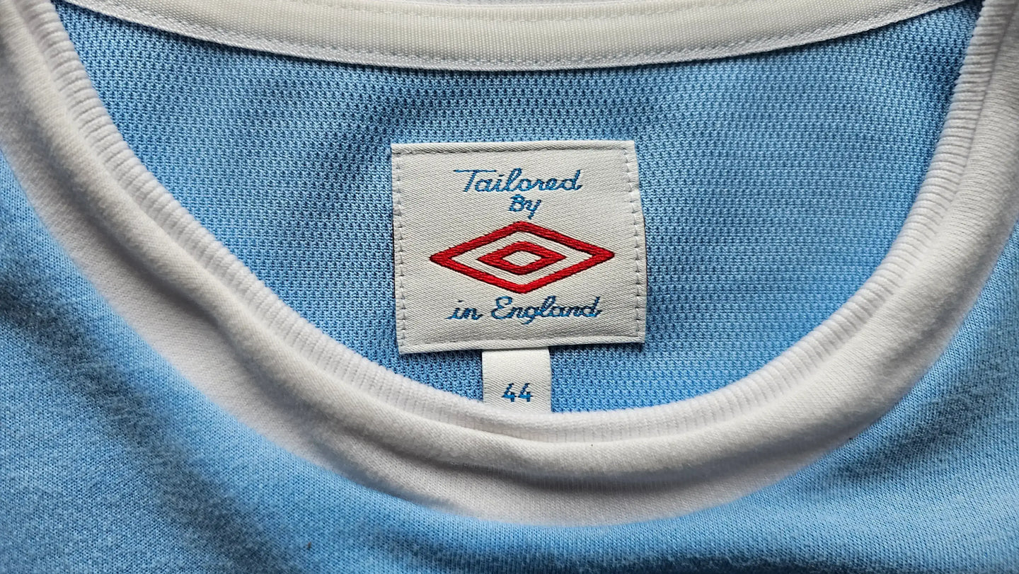 Label showing 'Tailored By Umbro' and size '44' on a blue background with white trim.
