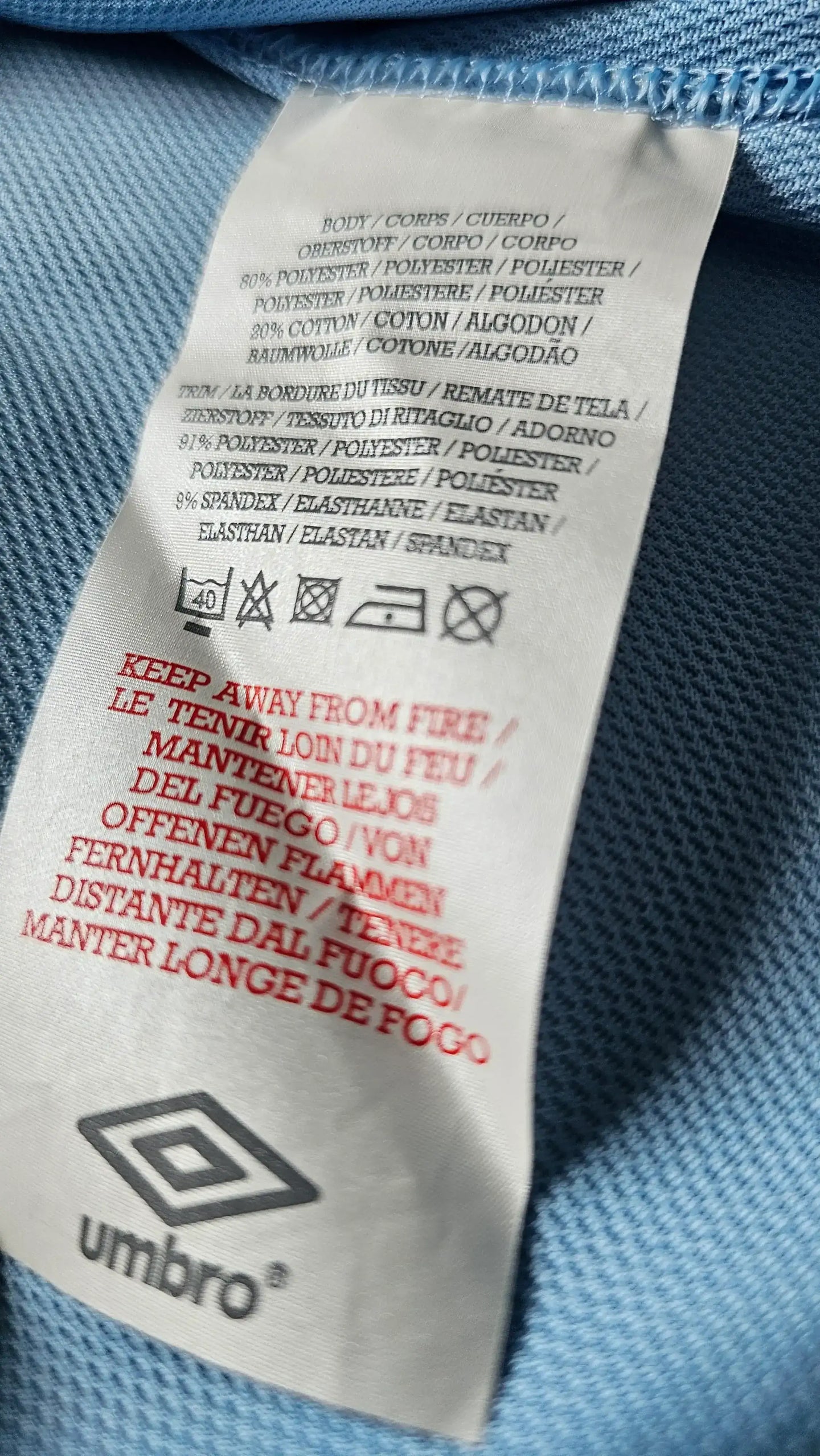 Care label detailing fabric composition with a warning to keep away from fire, and Umbro logo.