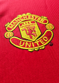 Close-up of Manchester United crest featuring the club name and emblem on a red background.