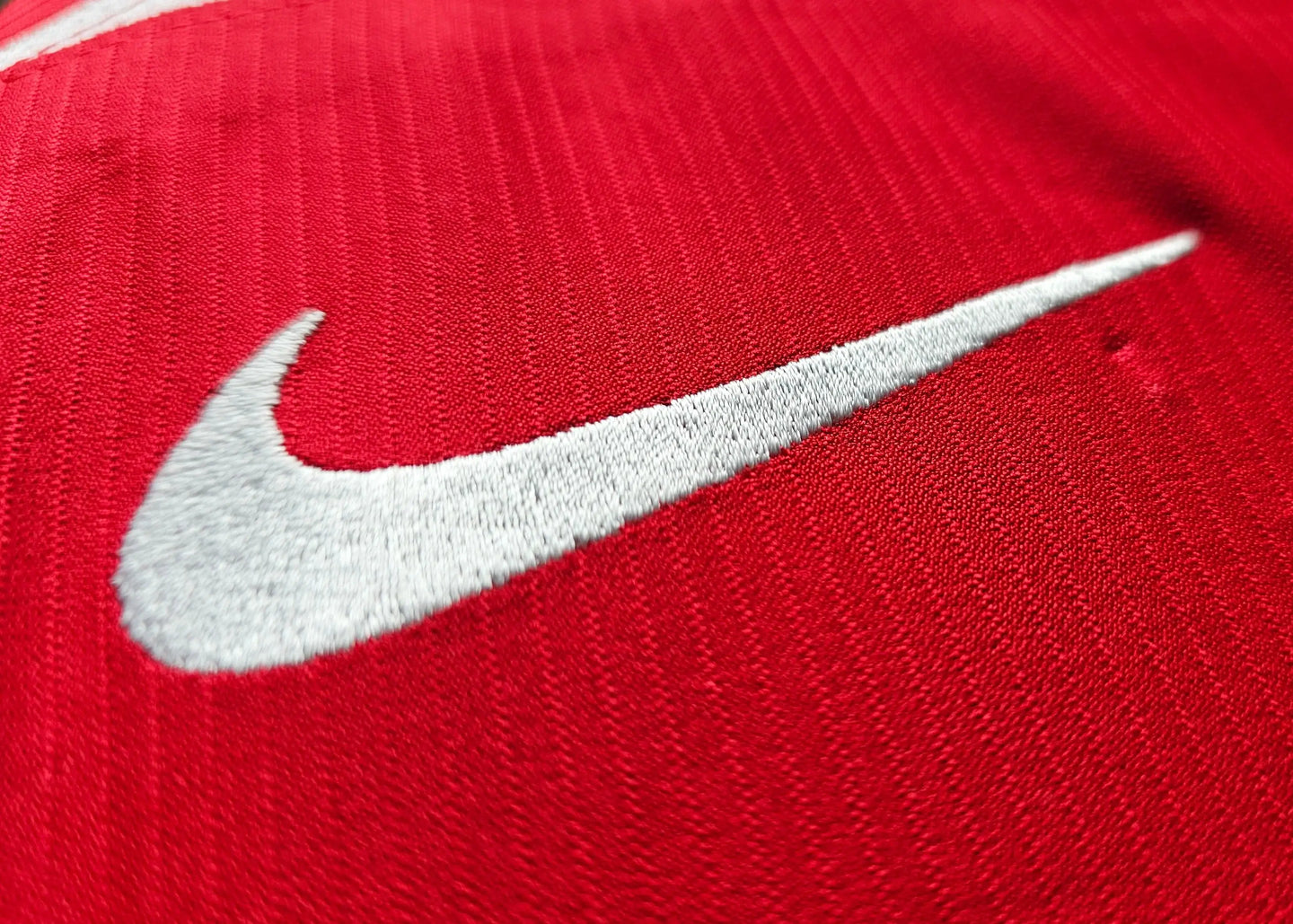 Close-up of the embroidered Nike logo on a red soccer jersey.