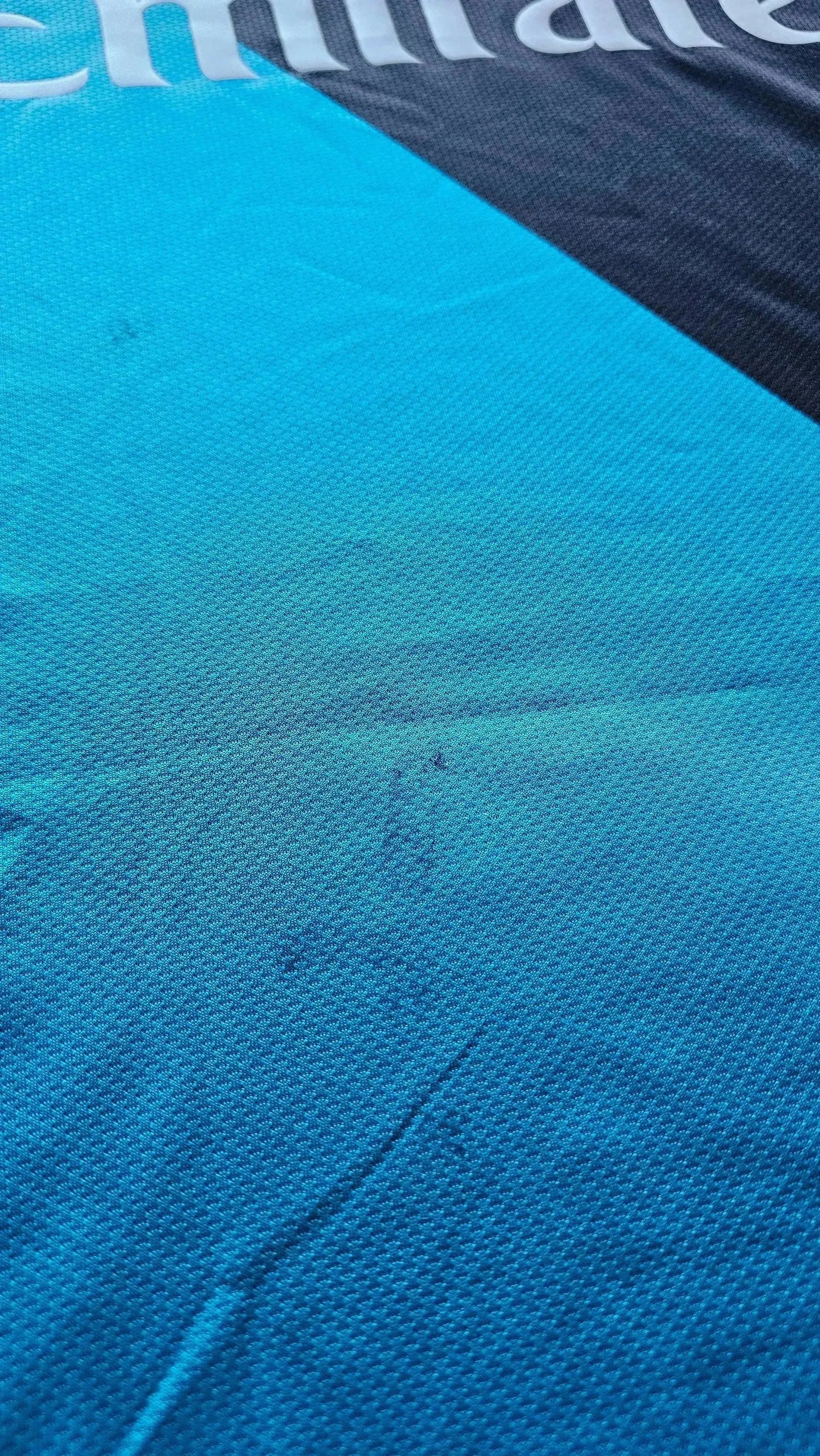 Detail showing the blue fabric of the Arsenal F.C. jersey with Emirates sponsor logo.