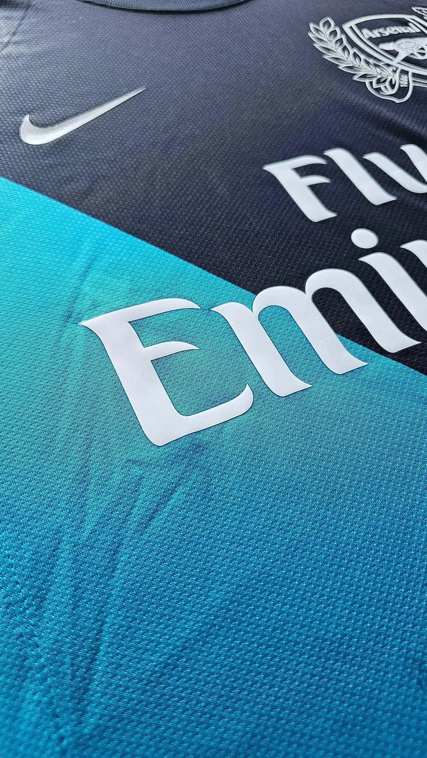 Close-up of Arsenal crest, Nike logo, and 'Fly Emirates' branding on Robin van Persie soccer jersey.