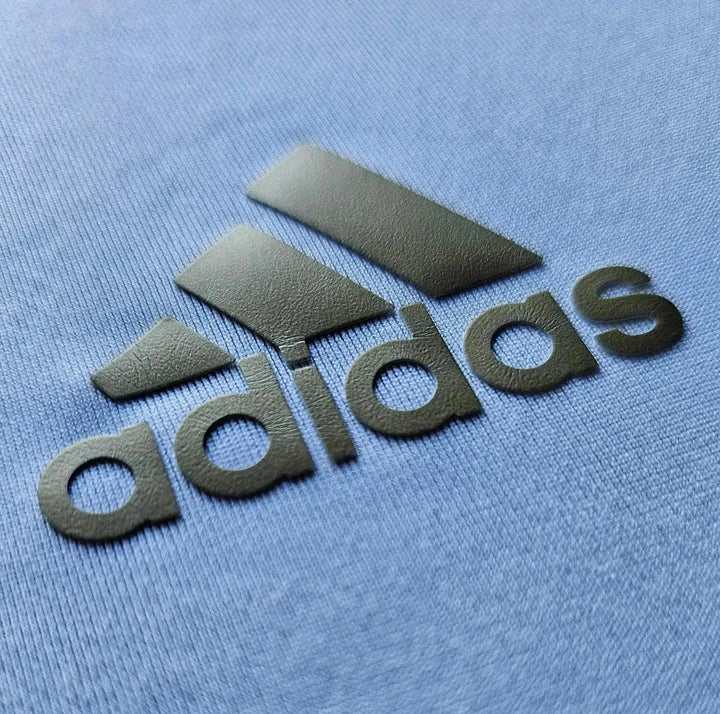 Close-up of the full adidas wordmark and logo embossed in dark olive on the light blue fabric of Gonzalo Higuain's Real Madrid shirt.
