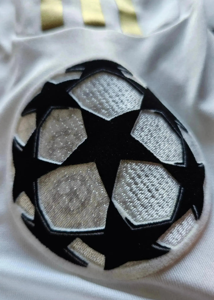 Close-up of the UEFA Champions League crest in black and white on a white football shirt.