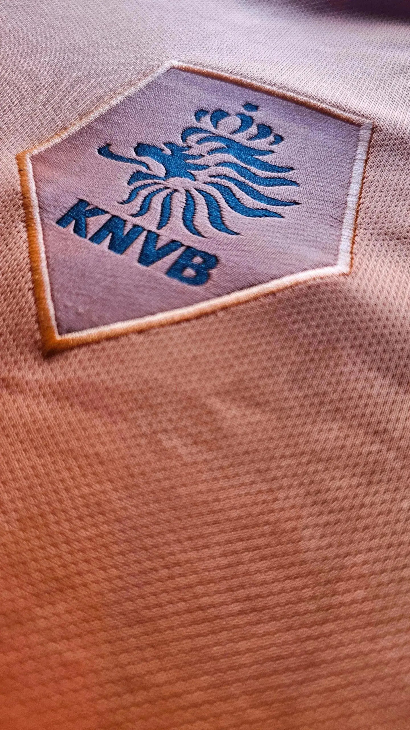 Crest detail featuring the KNVB logo in blue on an orange football shirt.