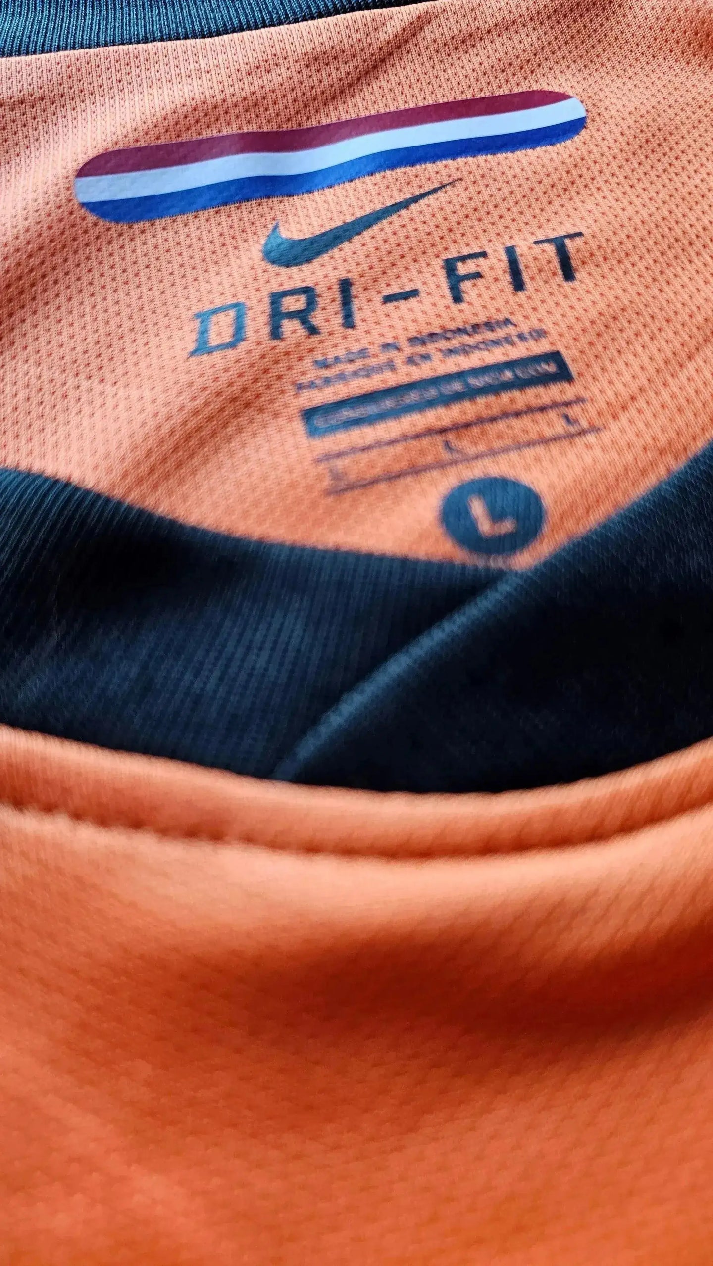 Close-up of the interior label showing DRI-FIT text and size L on an orange football shirt.