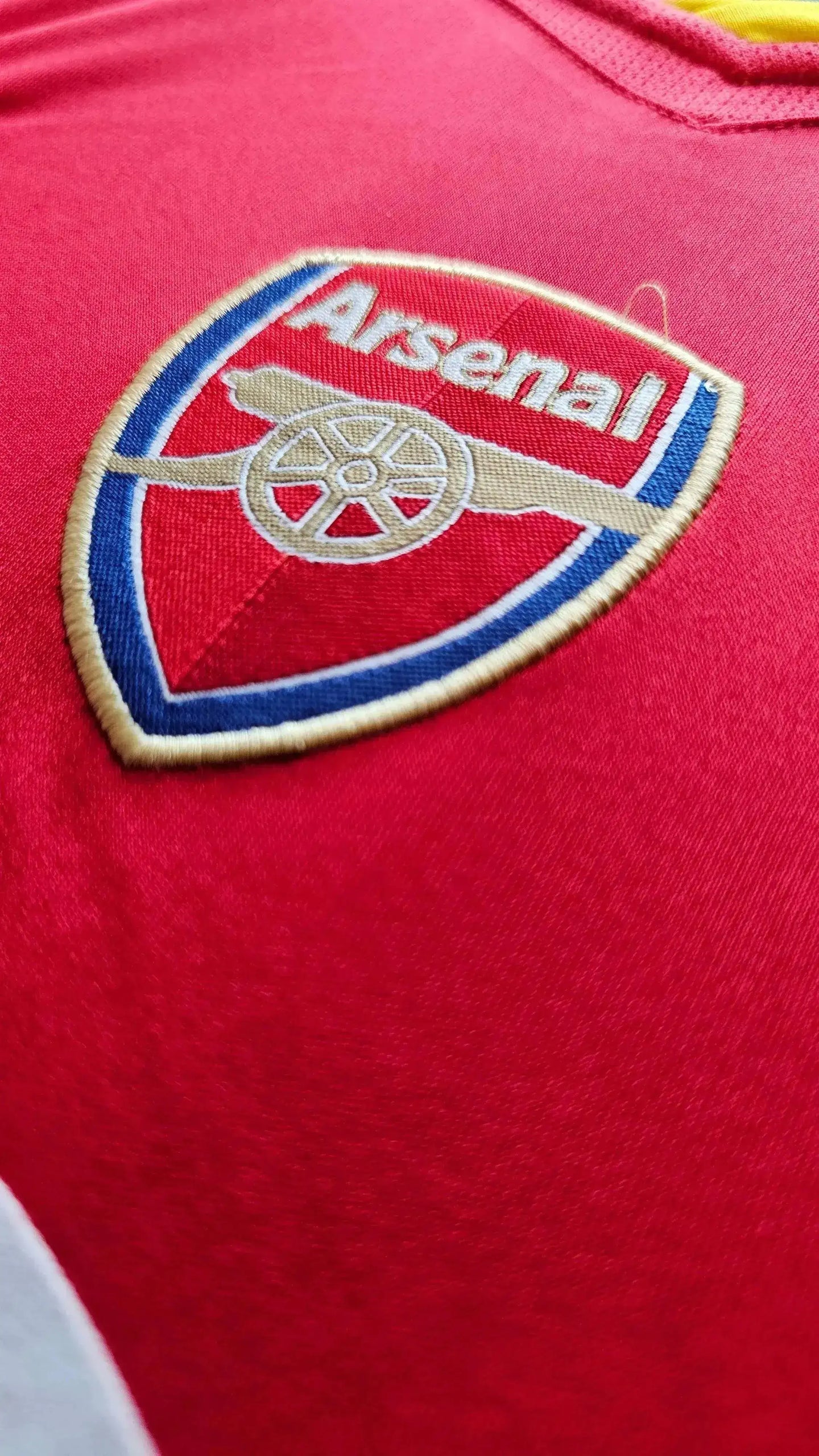 Close-up of the Arsenal crest on a red football shirt, featuring gold and blue details.