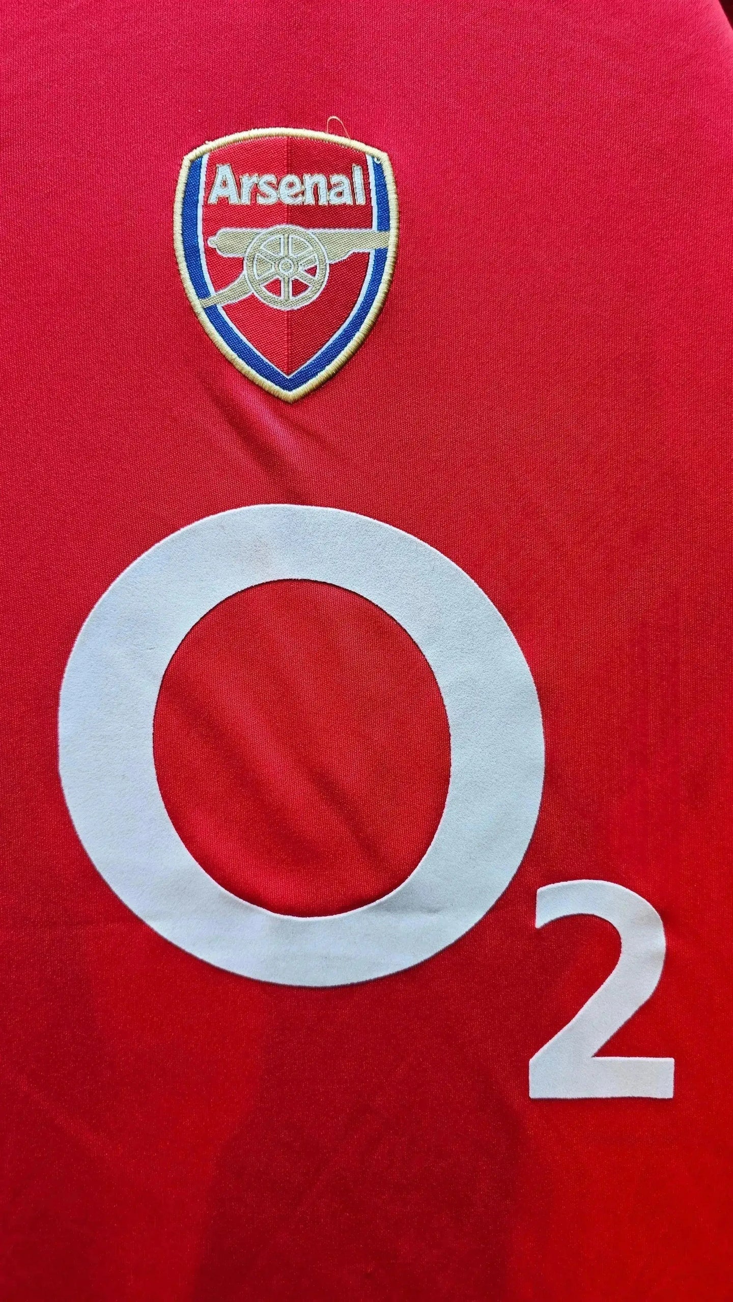 Arsenal crest and O2 sponsor on red background with a large white circle on the shirt.