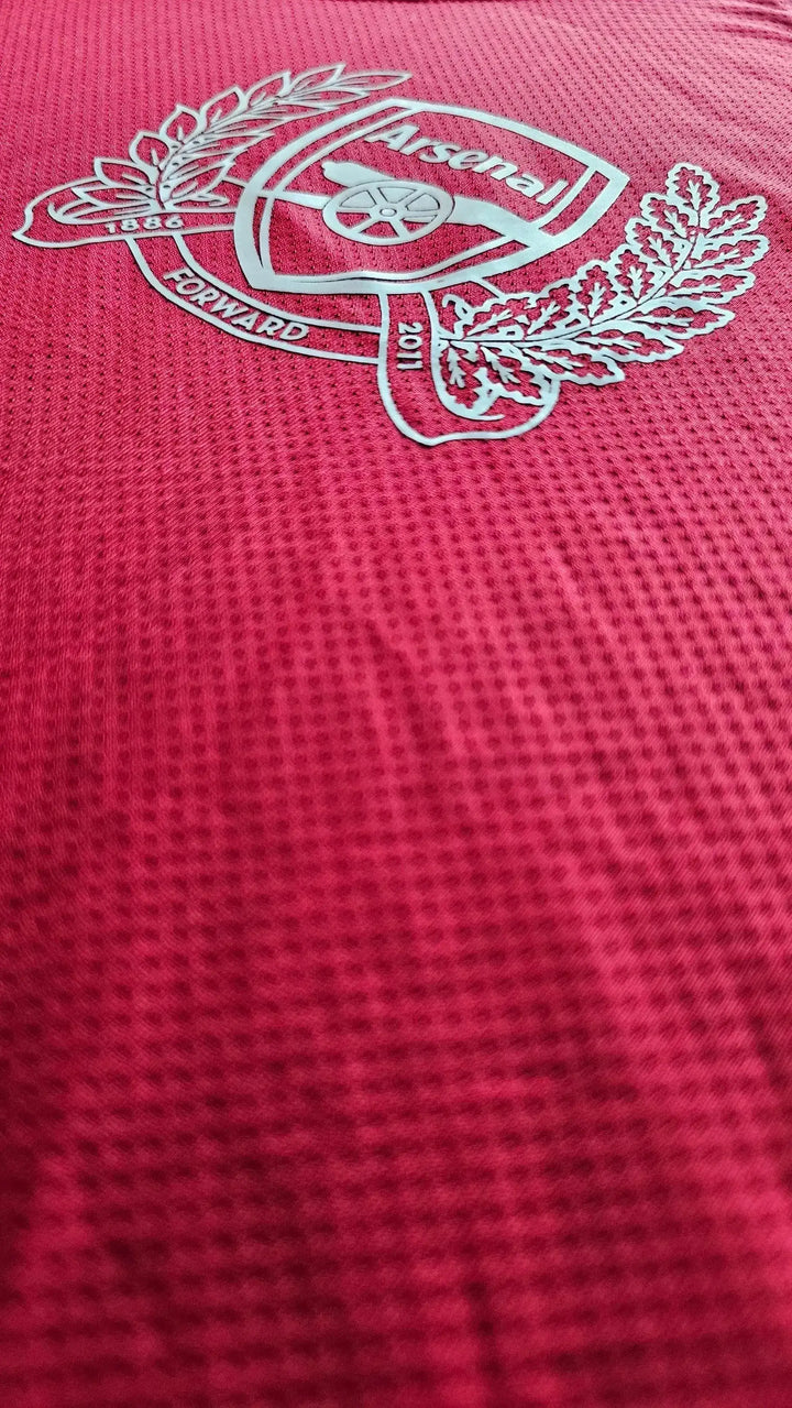 Crest detail of Arsenal F.C. with 1886, FORWARD, and 2011 in silver on a red background.