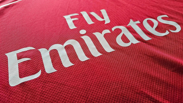 Close-up of 'Fly Emirates' sponsor text on a red Arsenal football shirt.
