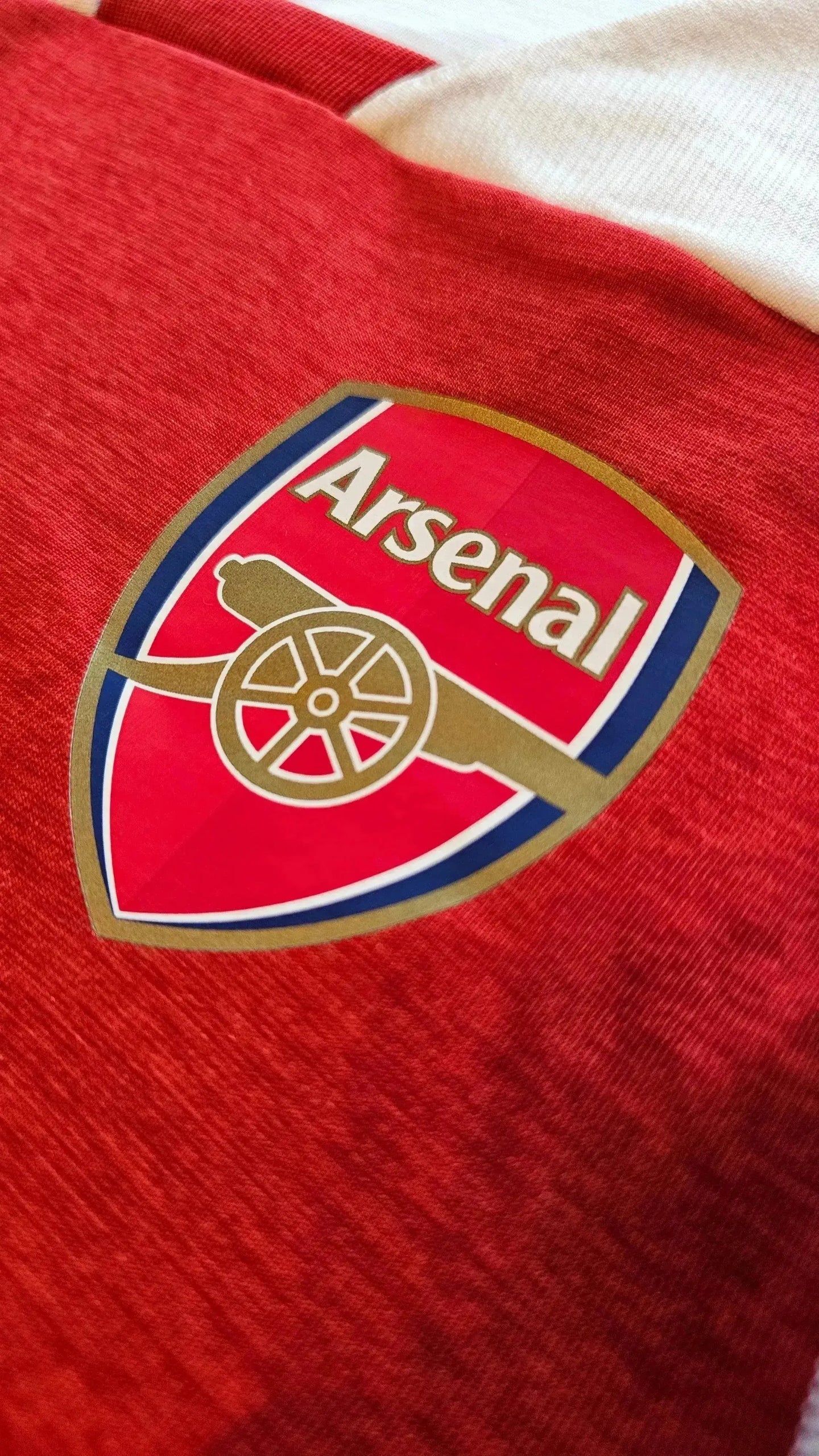 Close-up of Arsenal crest in red and white with gold accents on fabric.