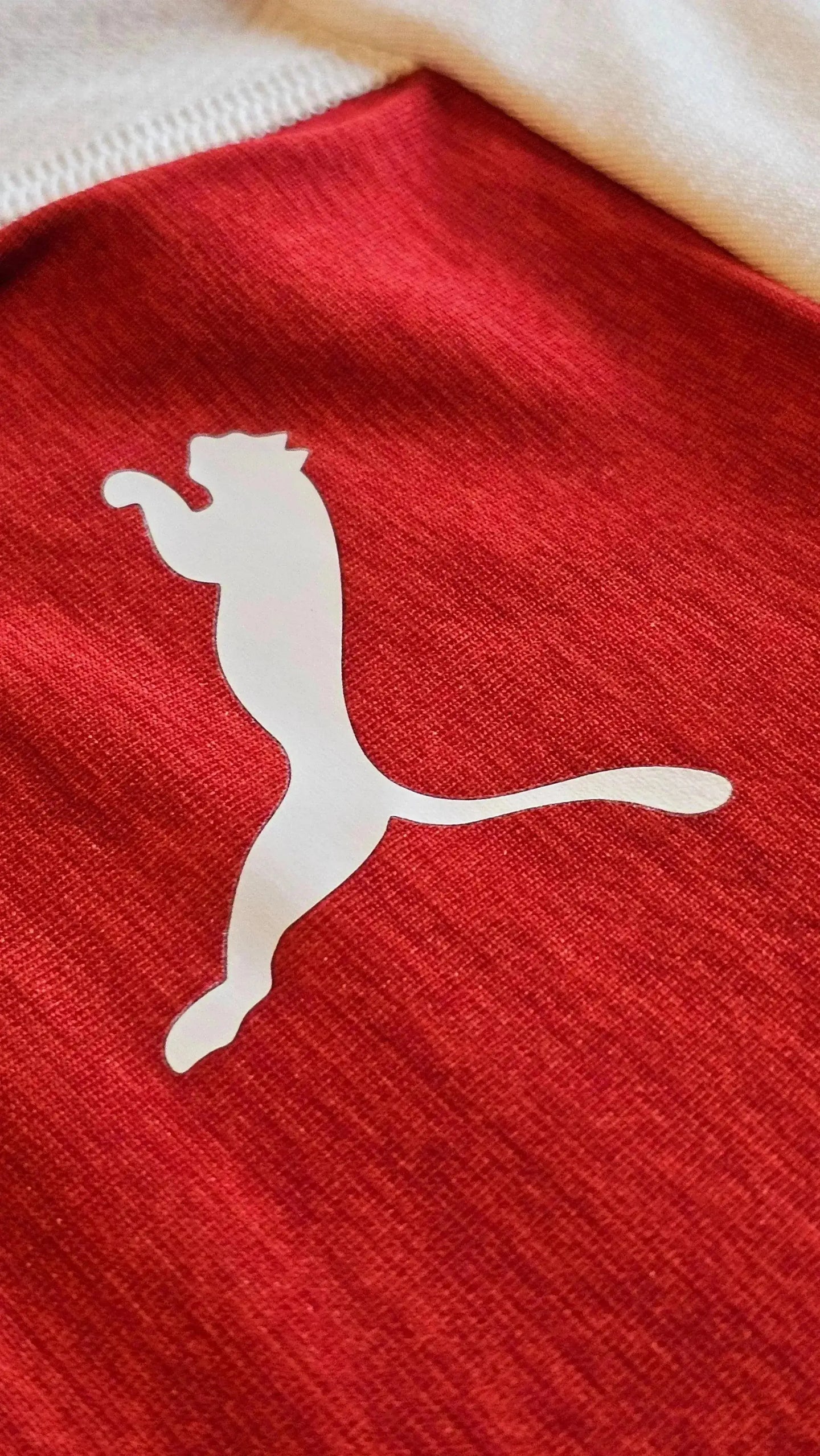 Close-up of white Puma logo on red fabric of soccer jersey.
