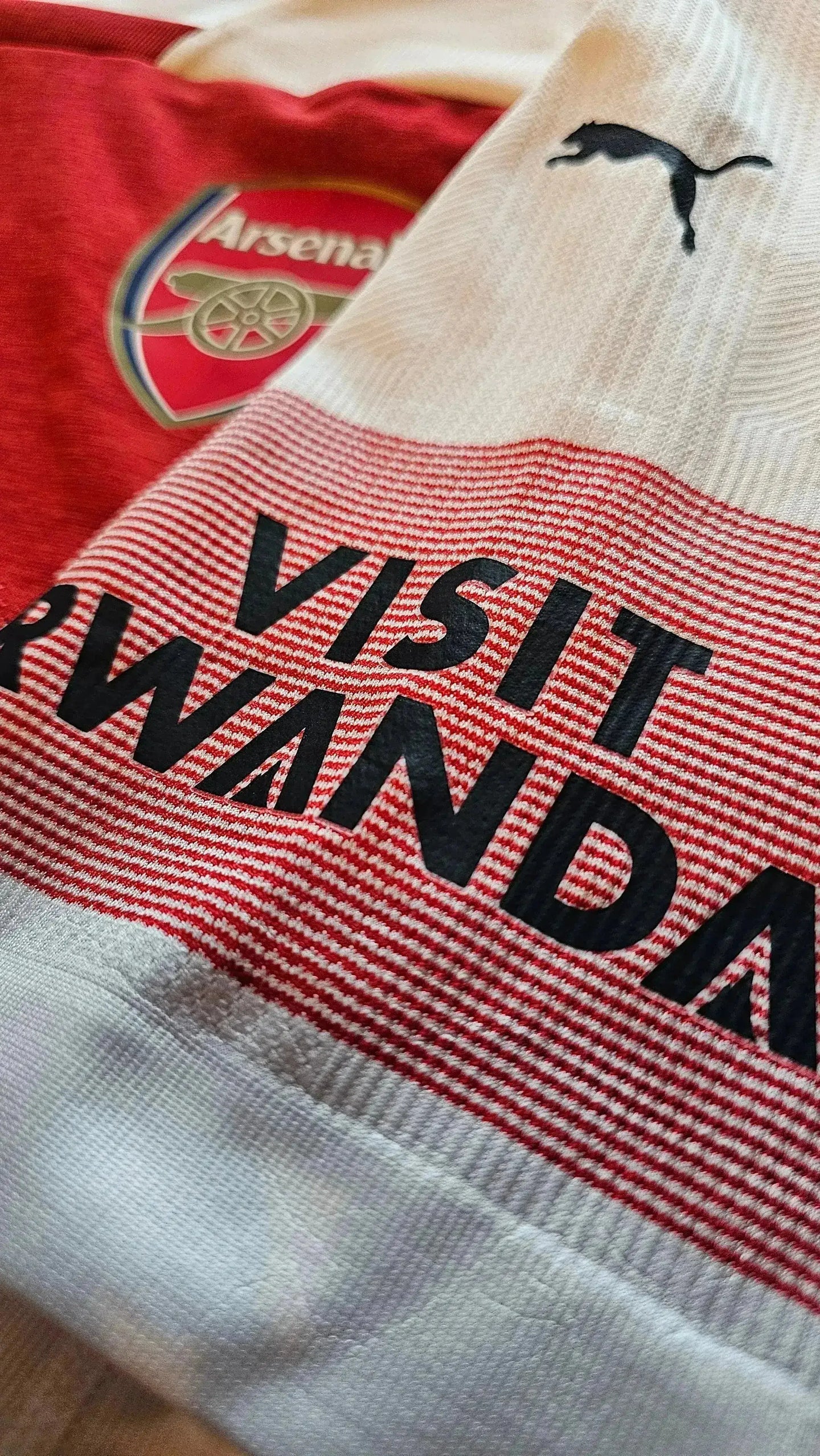 Detail showing Arsenal crest and black 'VISIT RWANDA' text on the soccer jersey.