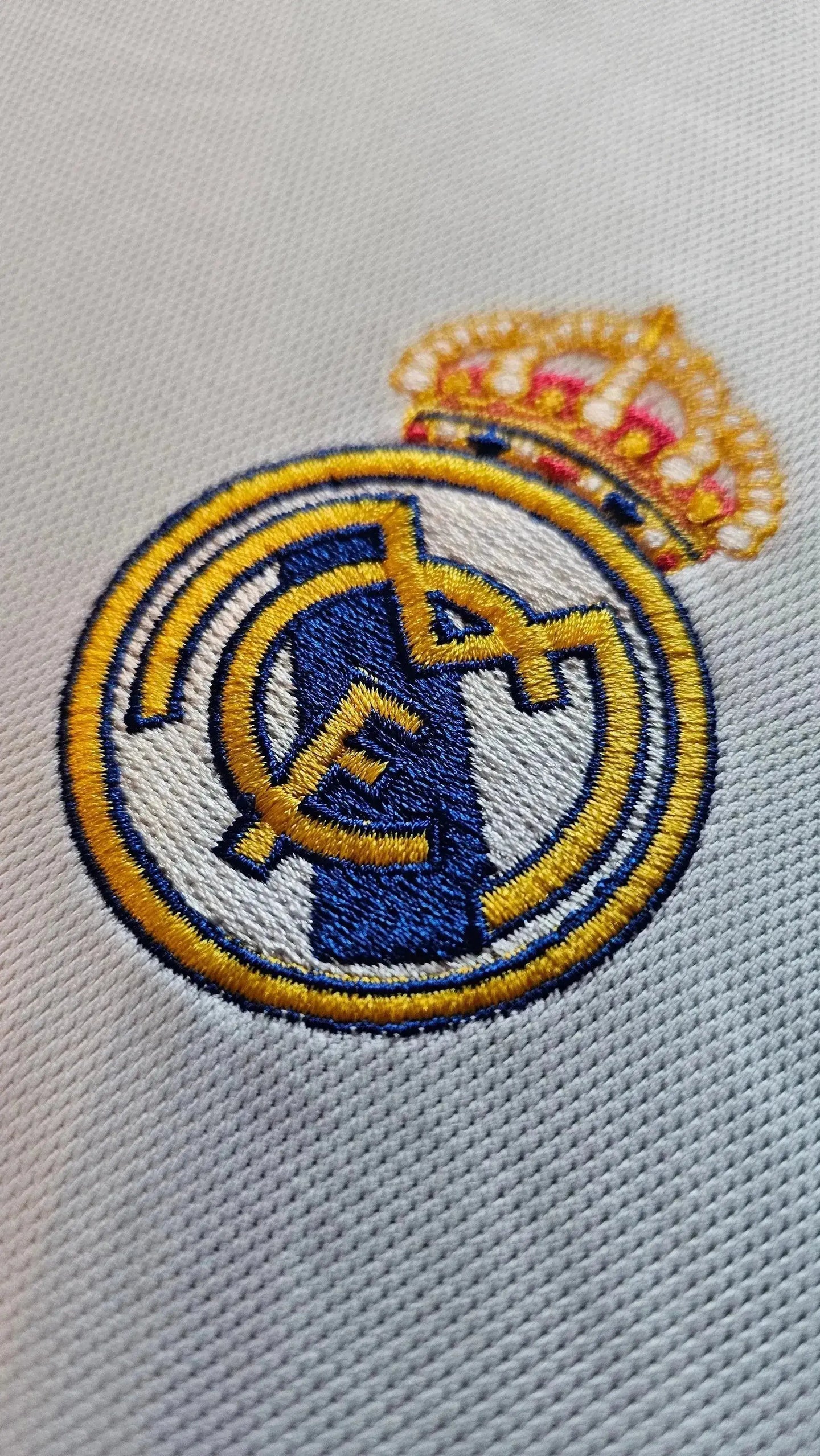 Crest detail of Real Madrid with golden crown and blue, white, and yellow embroidery.