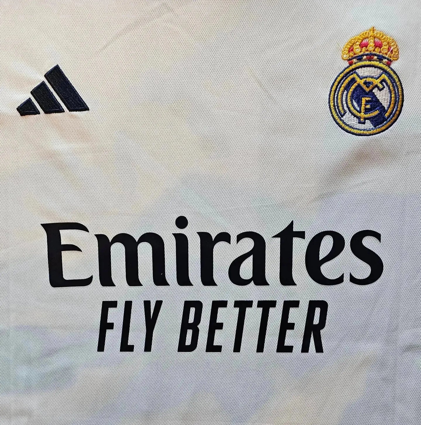 Detail view showing Real Madrid crest, adidas logo, and Emirates sponsor text on a white football shirt.