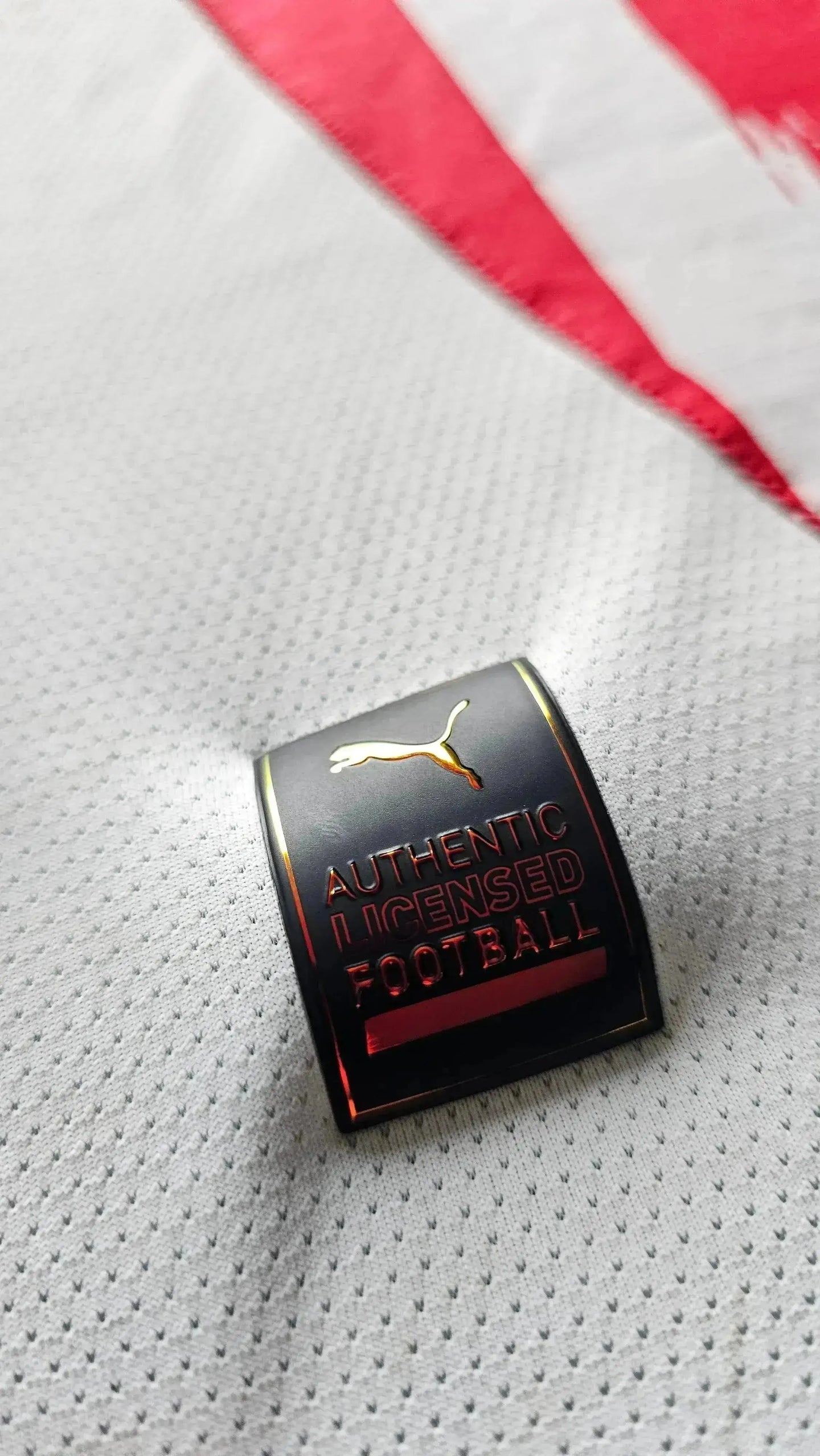 Close-up of the 'Authentic Licensed Football' tag with Puma logo on a white and red football shirt.