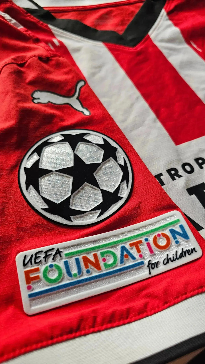 Detail view showing UEFA Foundation for children logo and Champions League badge on a red football shirt.