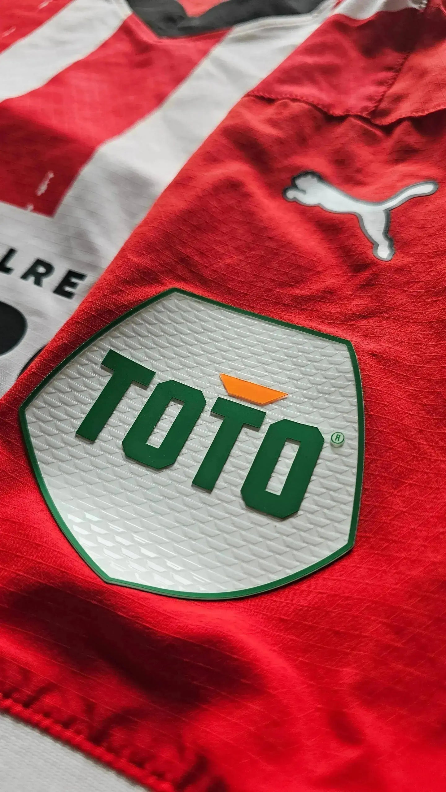 Detail view of the red football shirt featuring the TOTO sponsor logo and Puma branding.