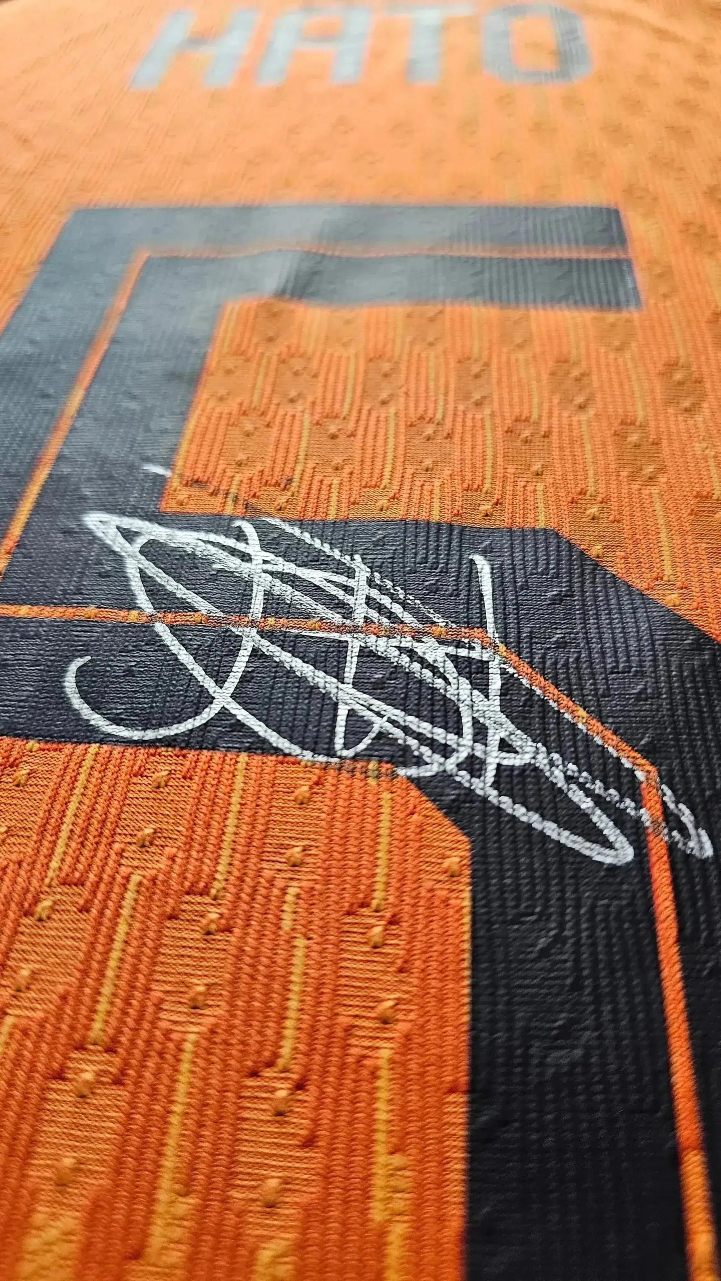 Signature detail of Jorrel Hato on an orange football shirt, featuring his name HATO.