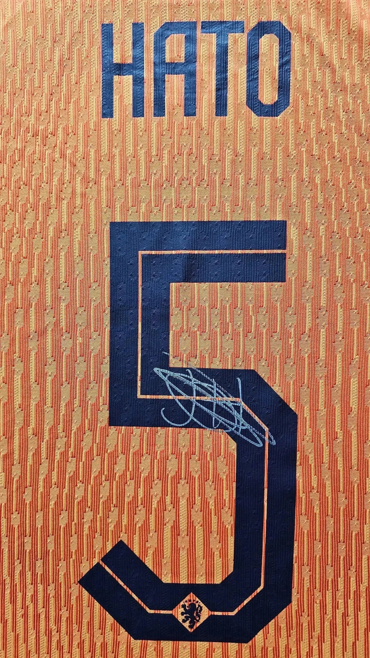Back view featuring player name HATO, No. 5, and signature detail on orange football shirt.