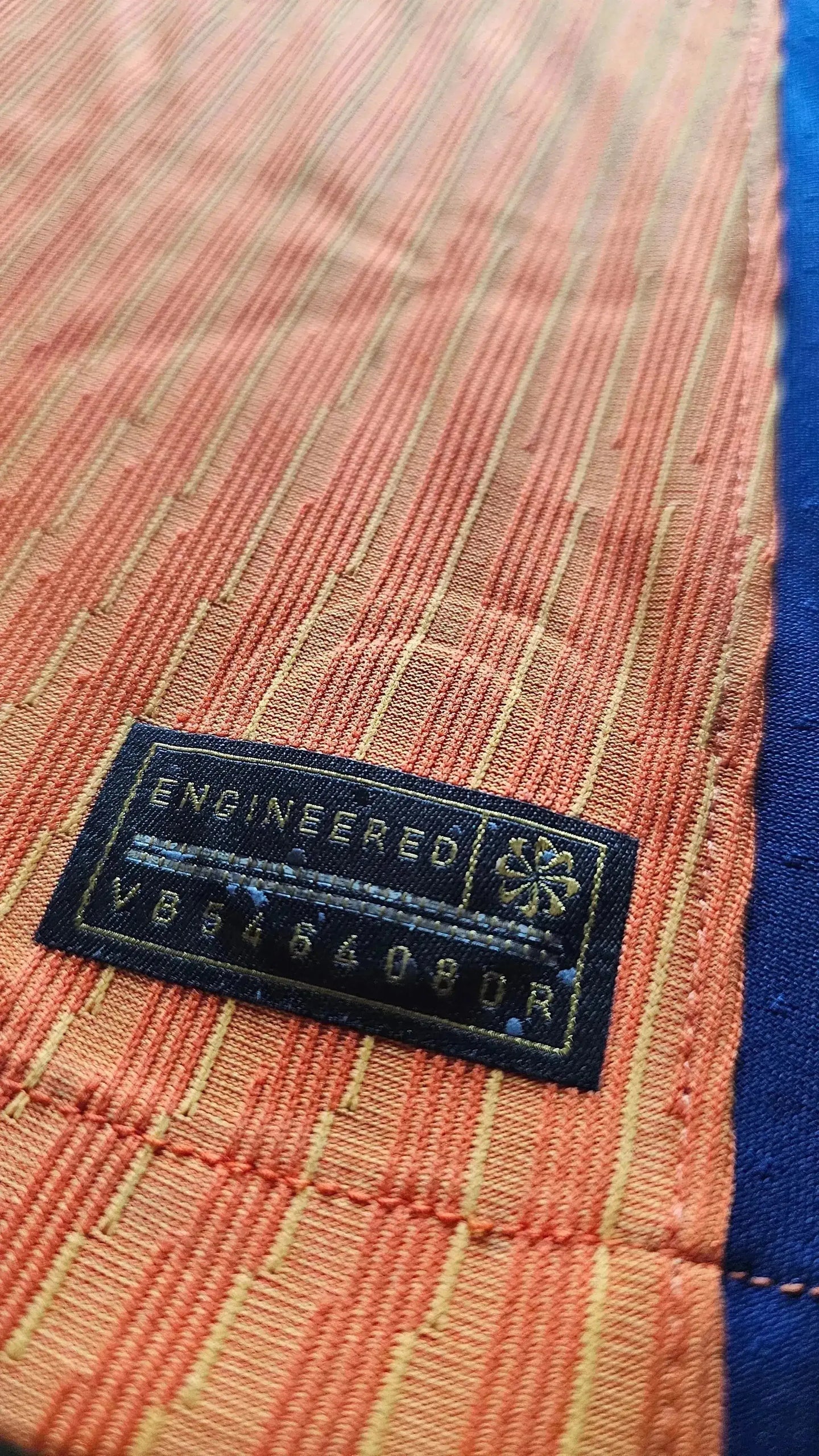 Close-up of the tag reading 'ENGINEERED' and code 'VB864089R' on an orange fabric.