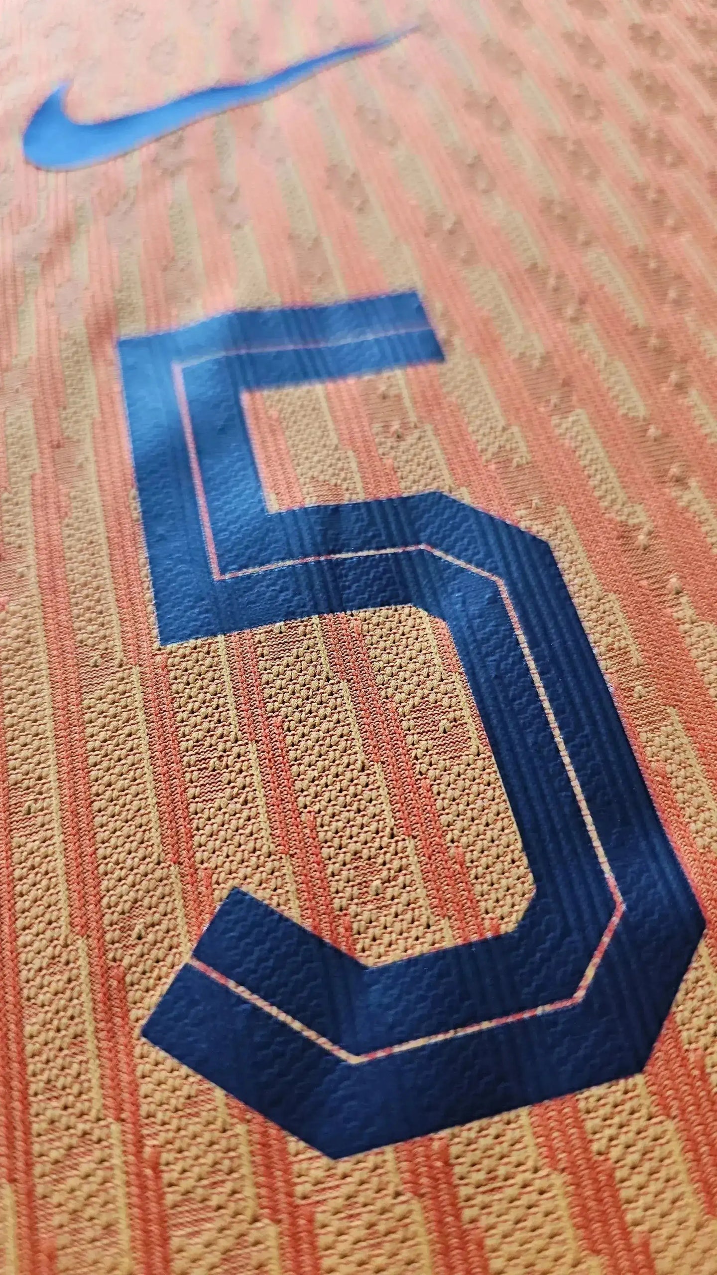 Close-up of No. 5 on football shirt with Nike logo in blue and orange pattern.