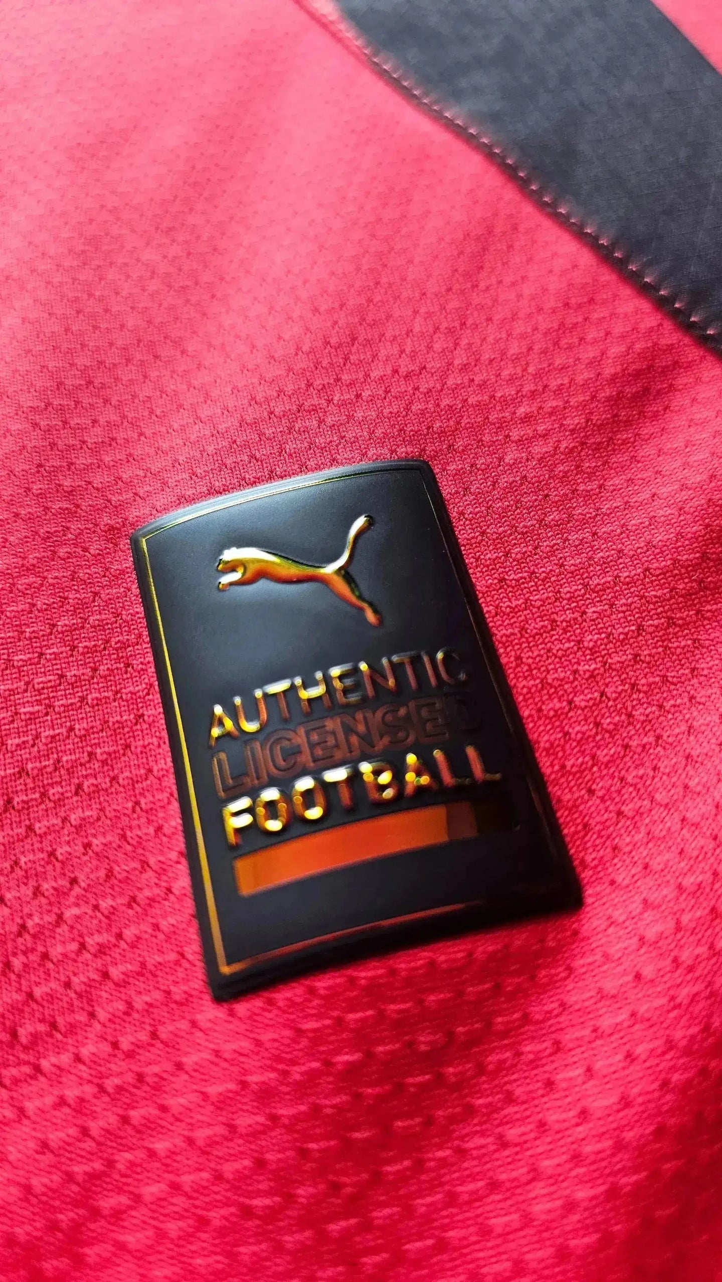 Close-up of the Puma logo and 'AUTHENTIC LICENSED FOOTBALL' text on a red fabric.