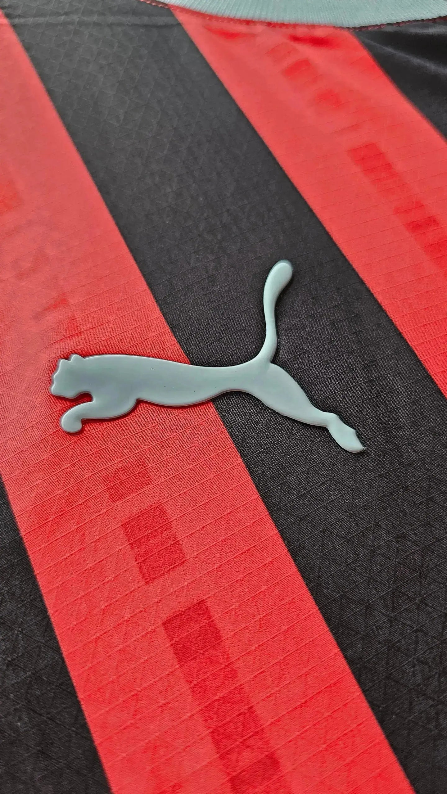 Puma logo on black and red striped fabric of football shirt.