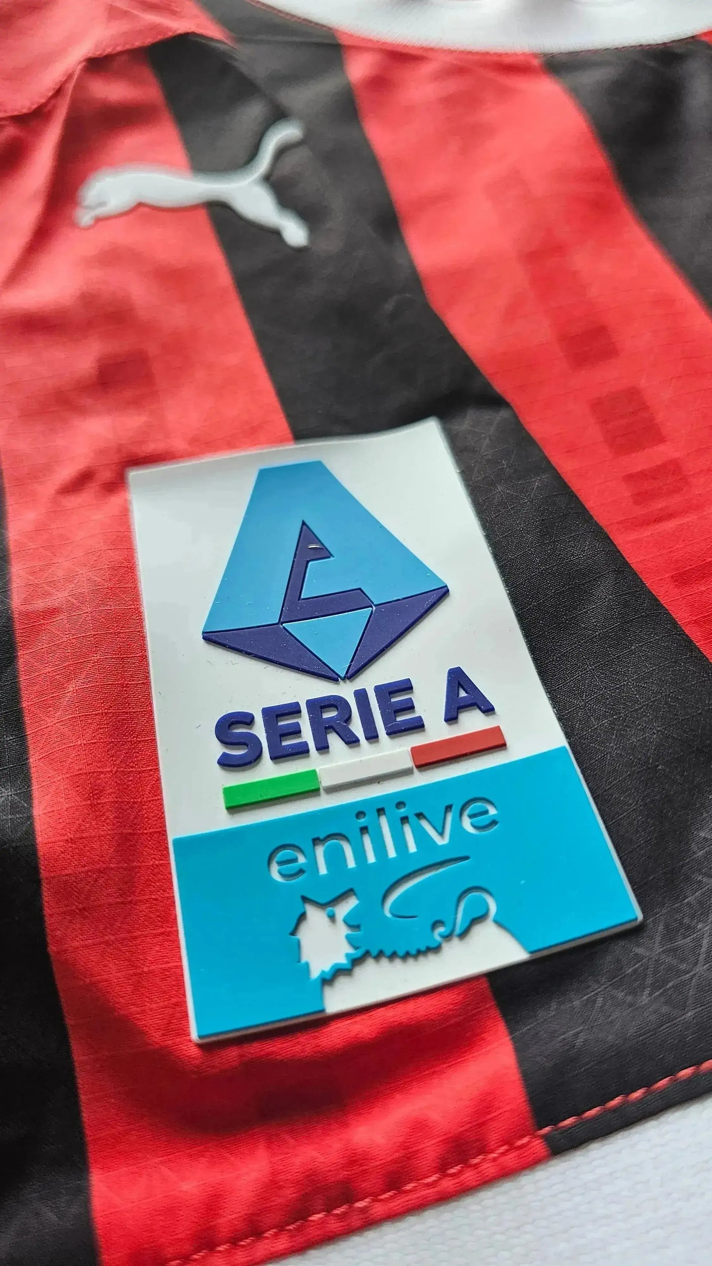 Close-up of Serie A badge with enilive text on red and black striped football shirt.