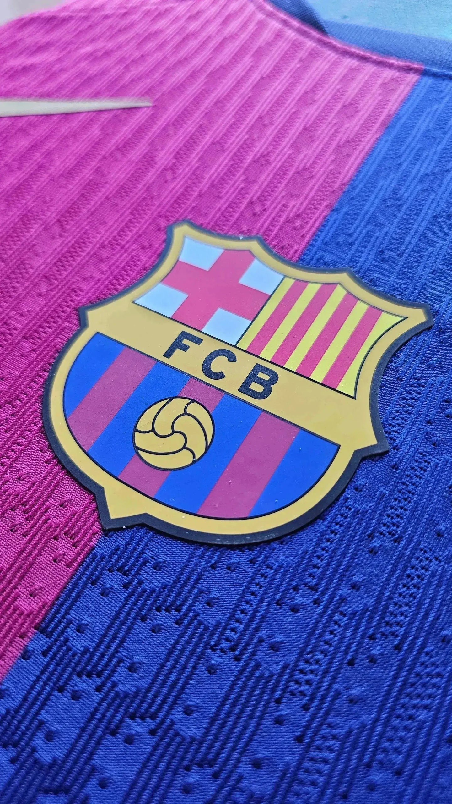 Close-up of the FC Barcelona crest on a pink and blue football shirt.