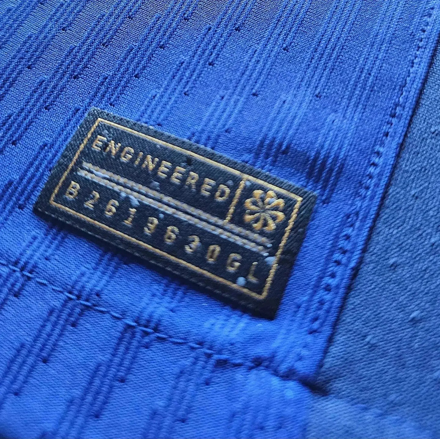 Detail view of the sizing label with ENGINEERED text and code B2619630GL on blue fabric.